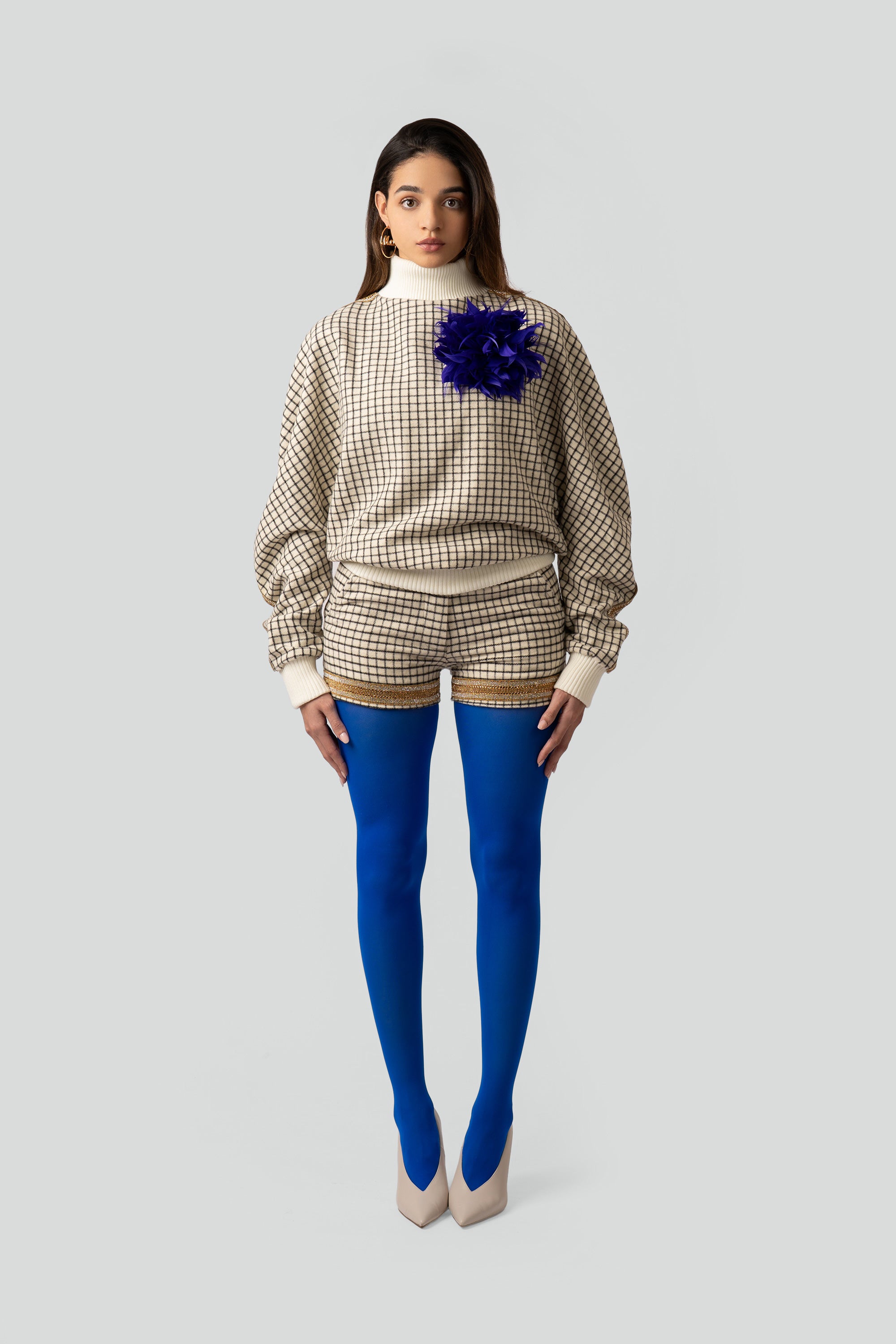 Woman wearing a grid patterned sweater with matching shorts and blue tights on a white background