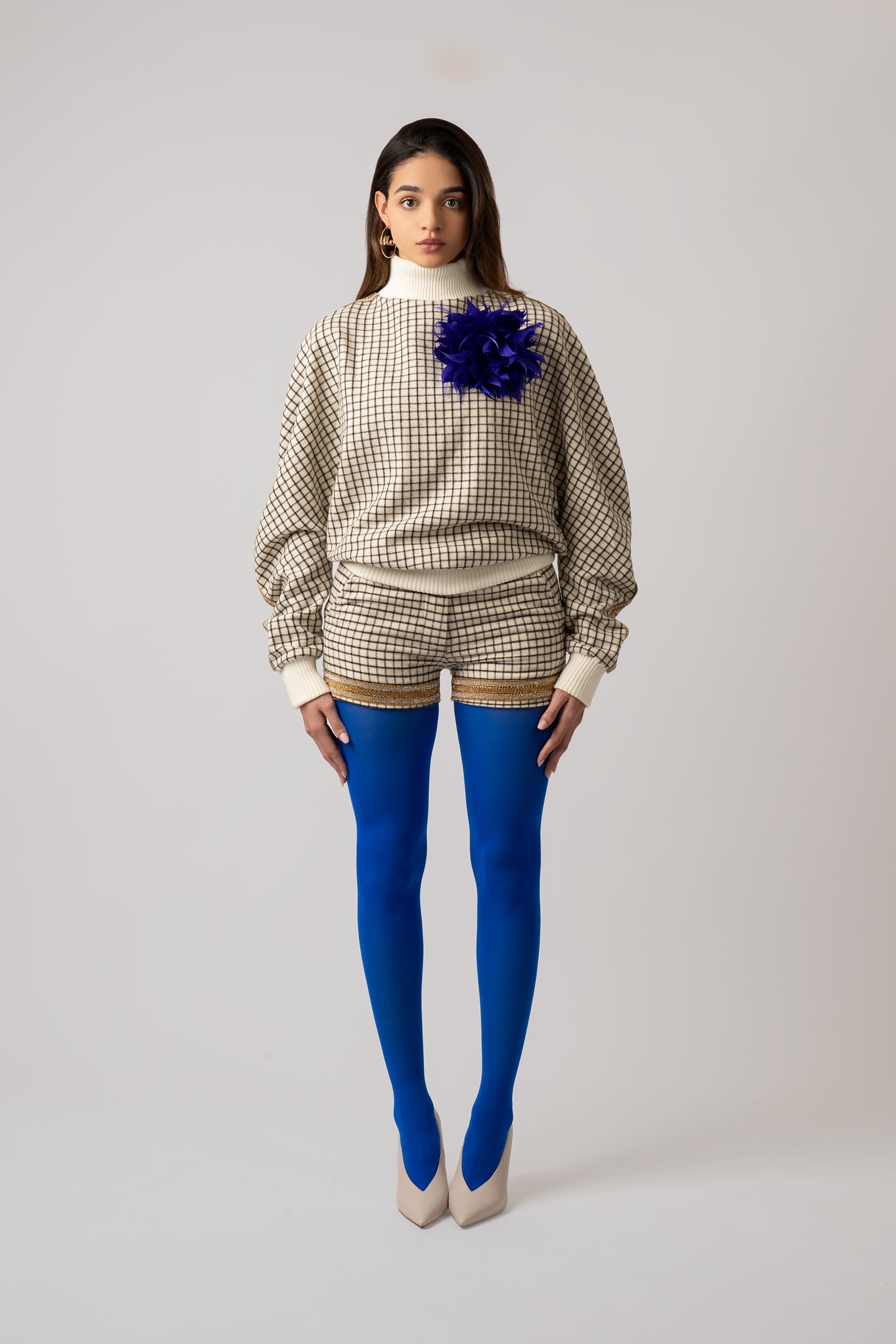 Woman wearing a grid patterned sweater with matching shorts and blue tights on a white background