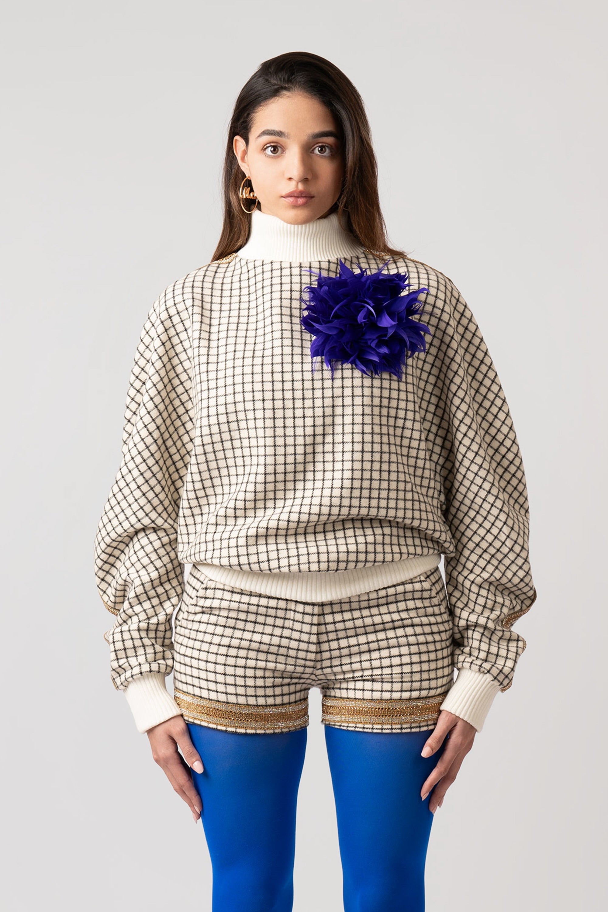 Woman wearing a grid patterned sweater with an indigo feathered brooch on a white background