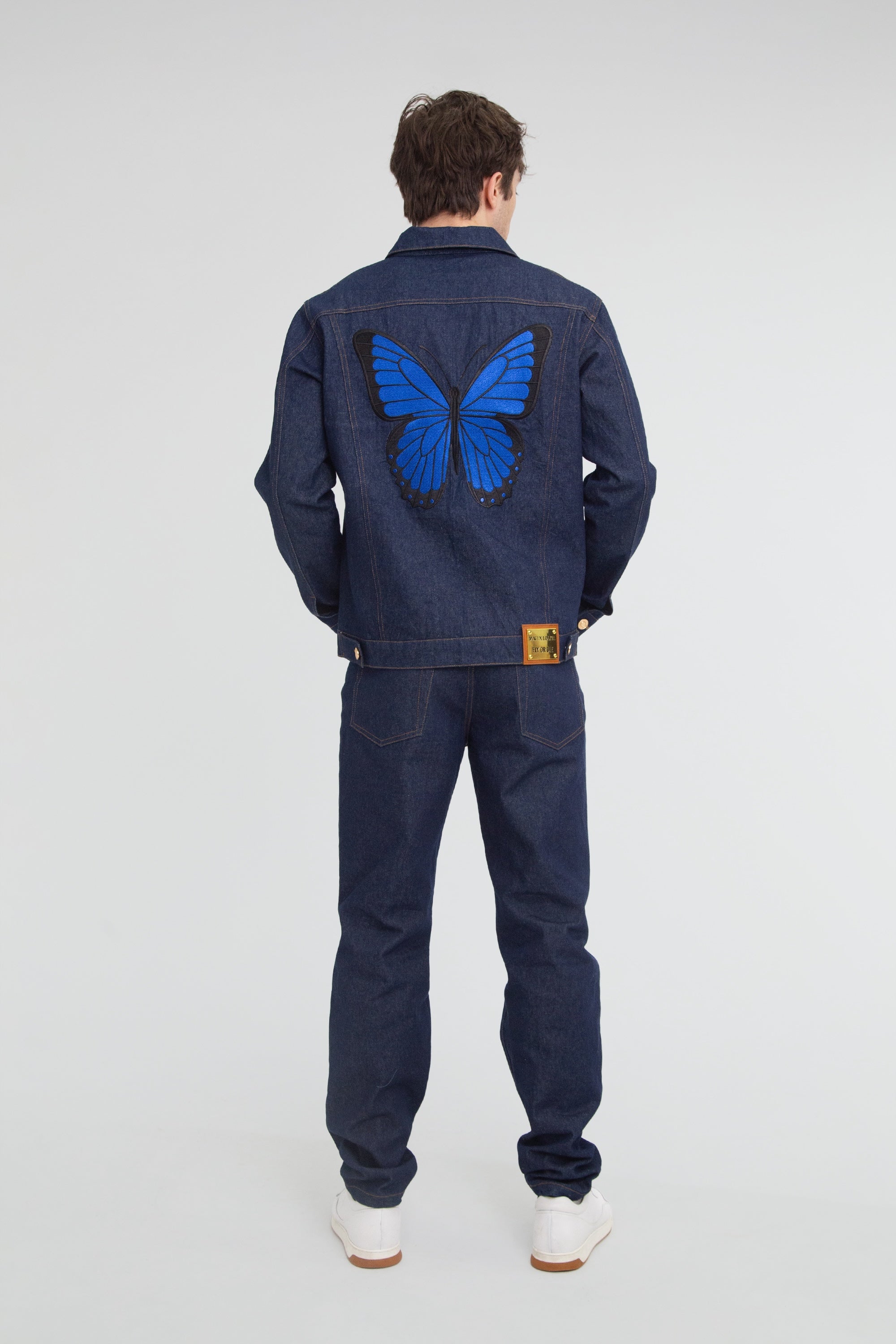 Person wearing a denim outfit with a blue butterfly design on the back, standing against a plain background.