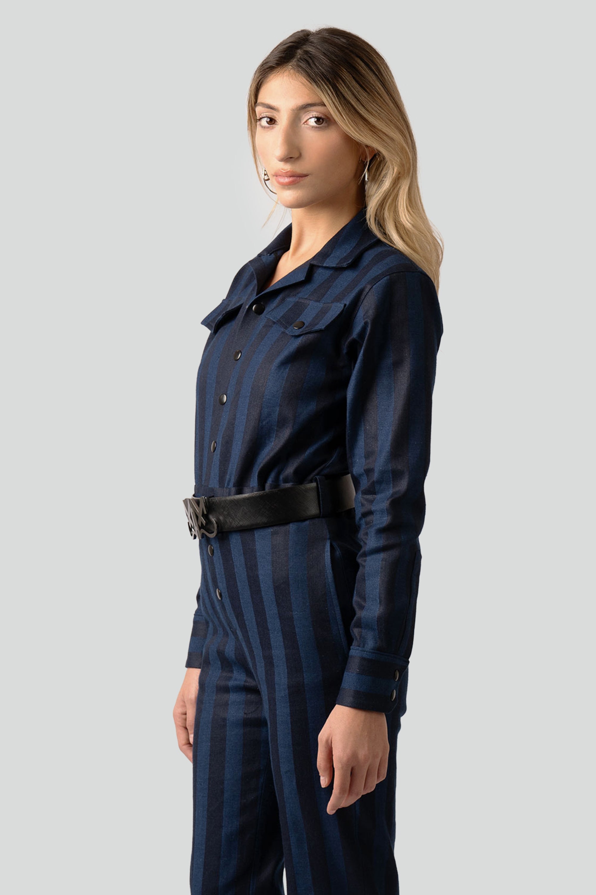 Woman wearing a navy blue striped jumpsuit with a belt on a white background