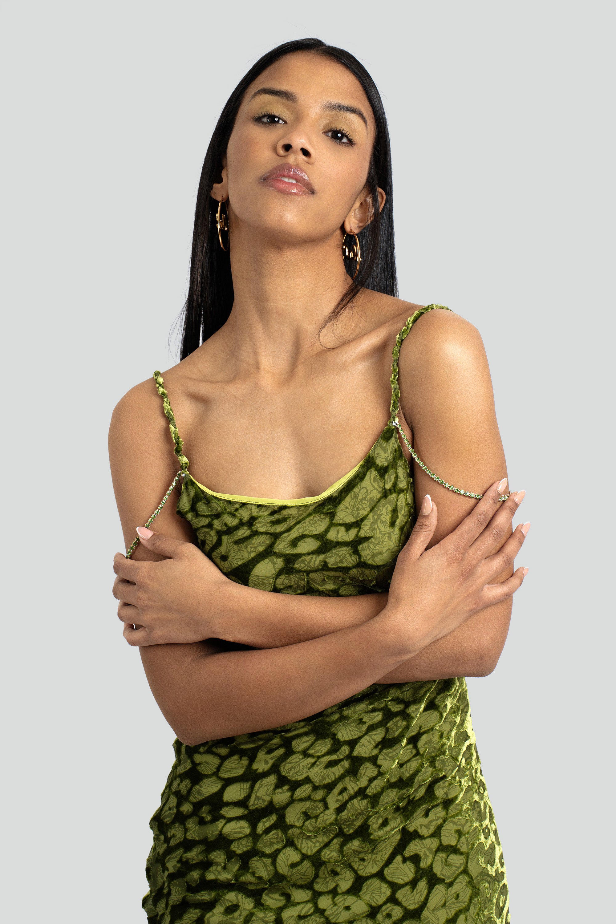 A woman wearing an olive green leopard imprint slip dress with crystal chain accent straps.