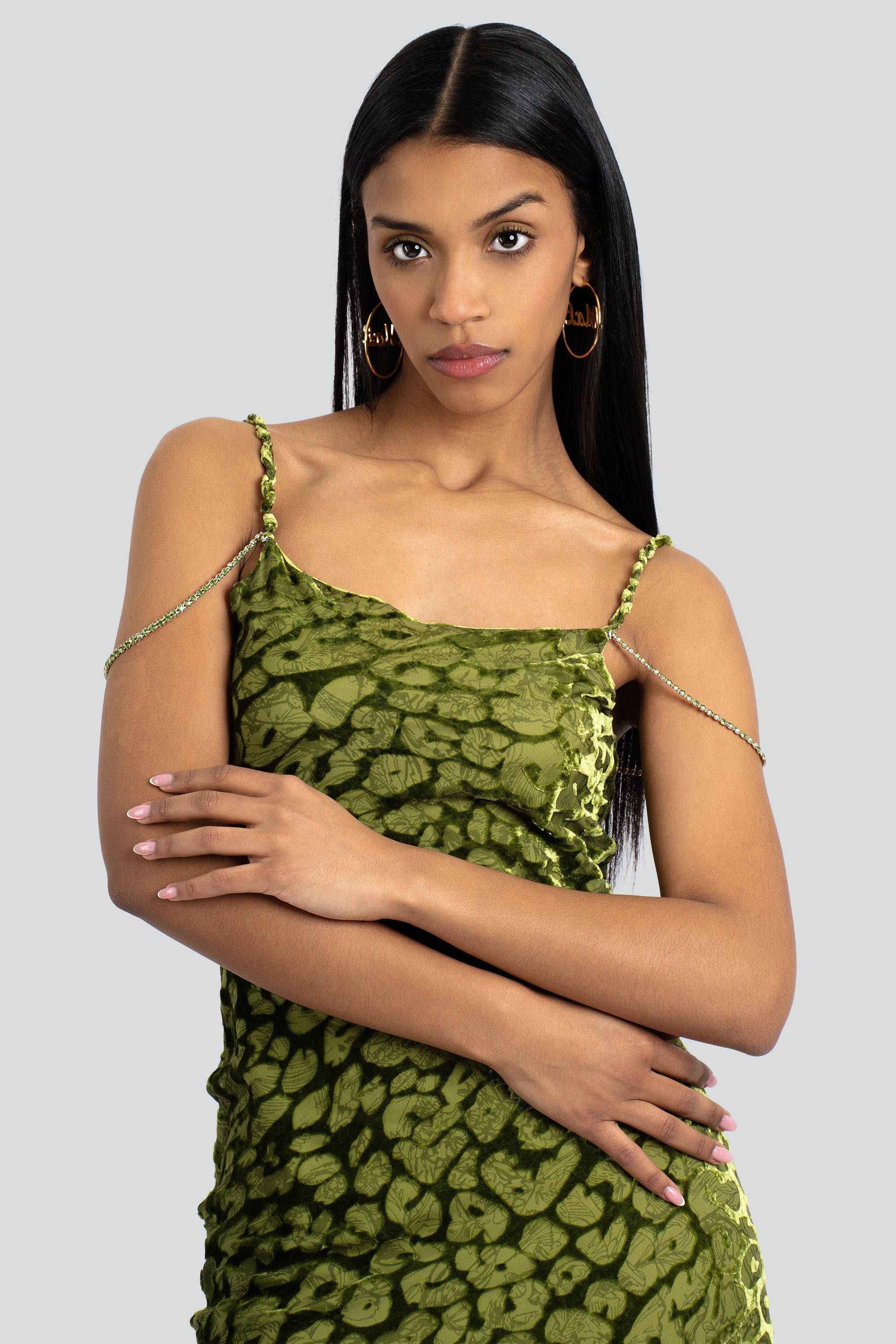 A woman wearing an olive green leopard imprint slip dress with crystal chain accent straps.