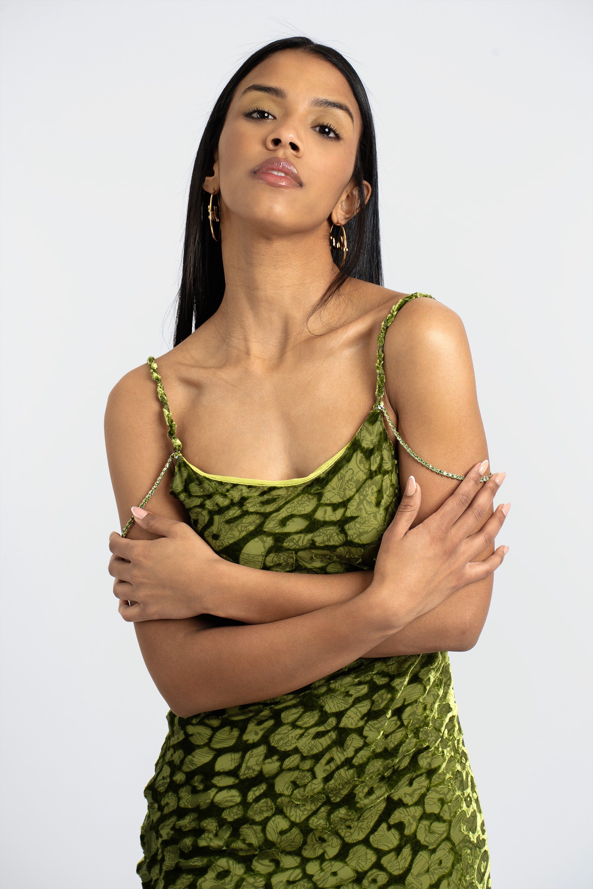 A woman wearing an olive green leopard imprint slip dress with crystal chain accent straps.