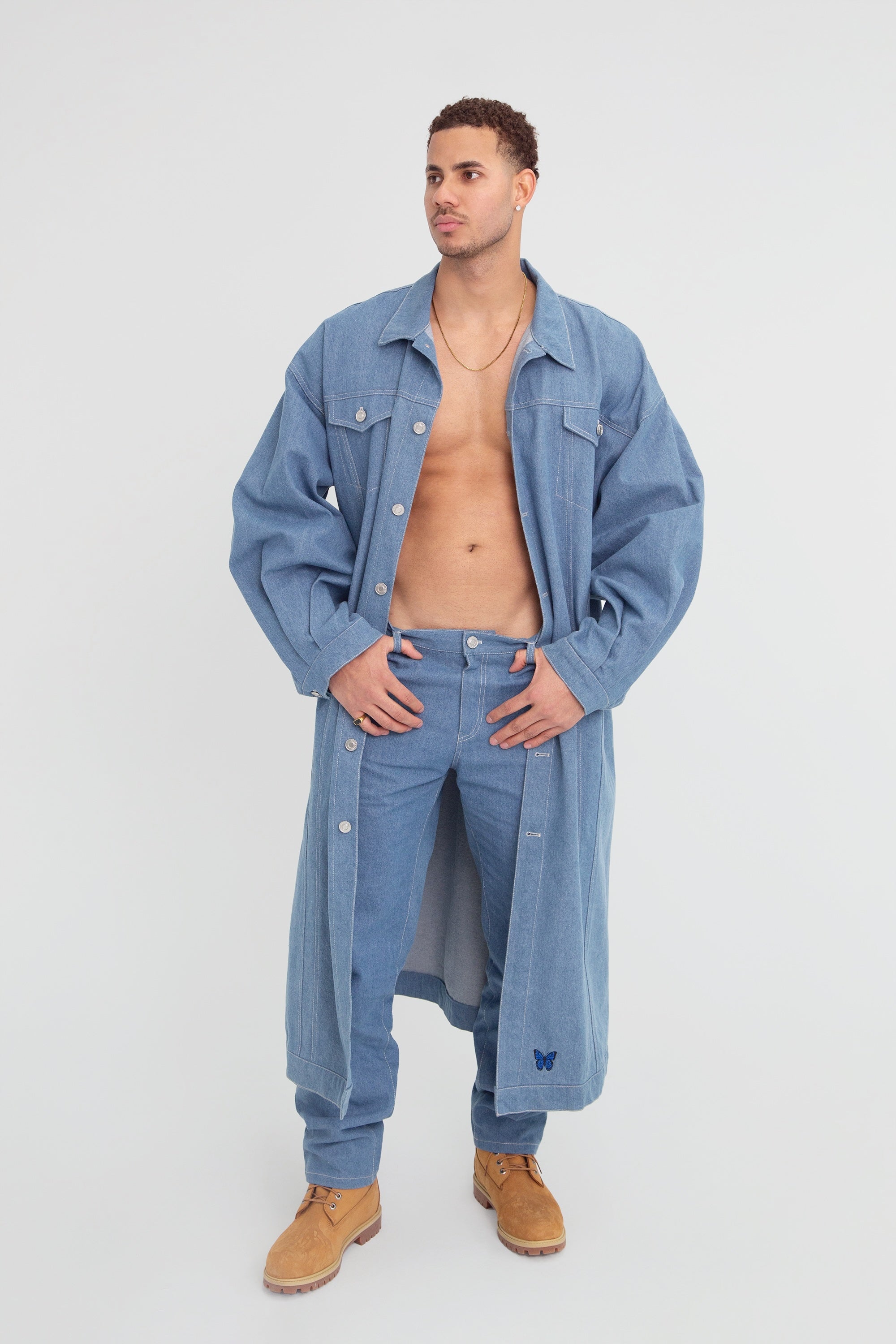 Man wearing a long oversized denim jacket and pants on a plain background