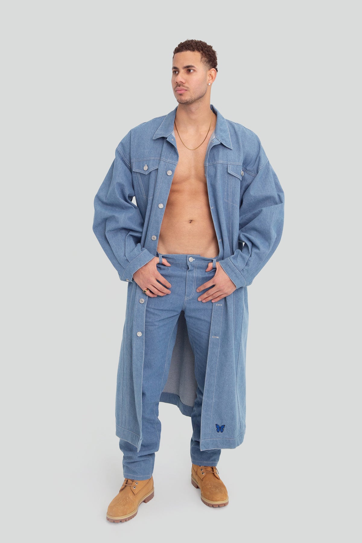 Man wearing a light wash oversized denim trench coat jacket featuring a structured longline silhouette and classic front button closures