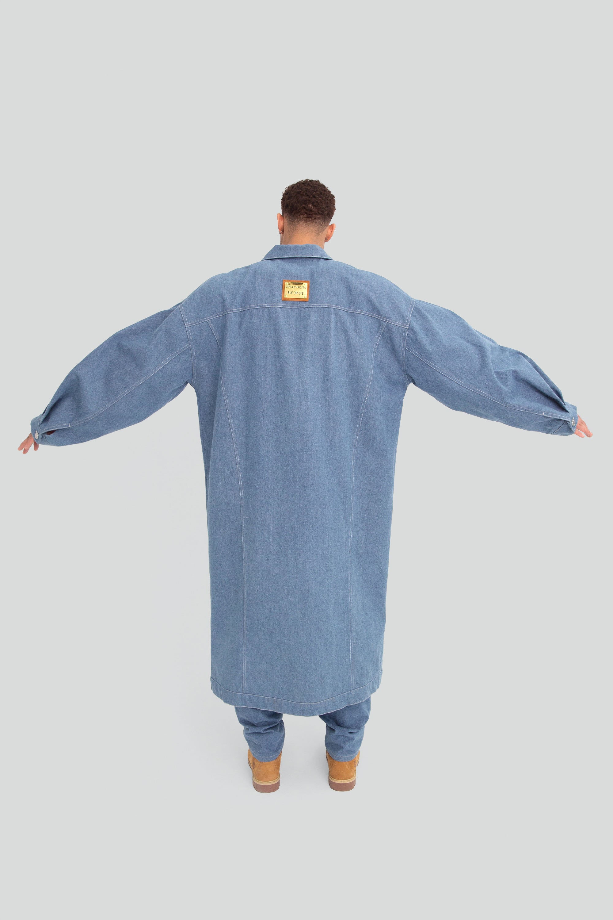 Man wearing a long oversized denim jacket on a plain background