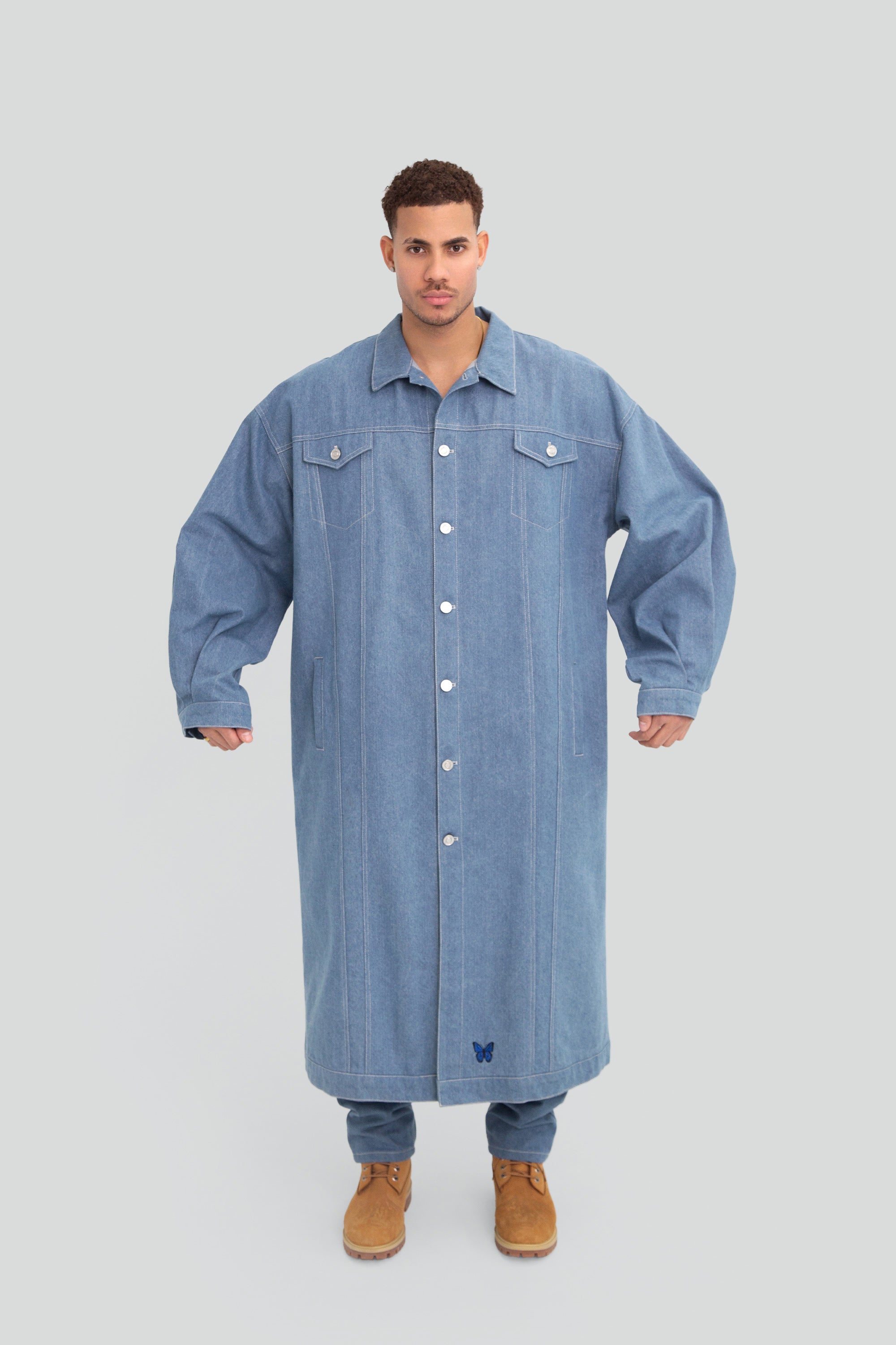 Man wearing a long oversized denim jacket on a plain background