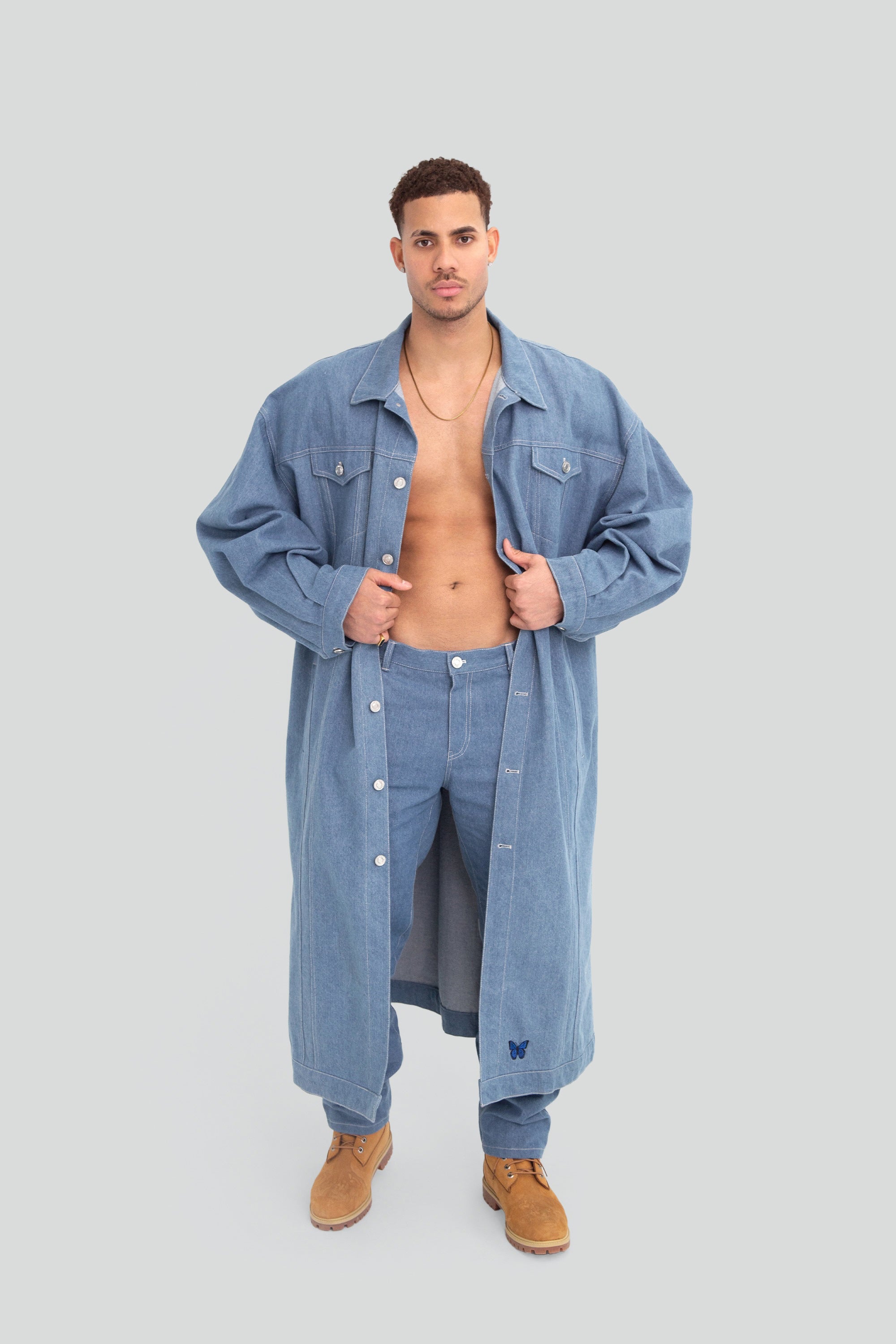 Man wearing a long oversized denim jacket and pants on a plain background