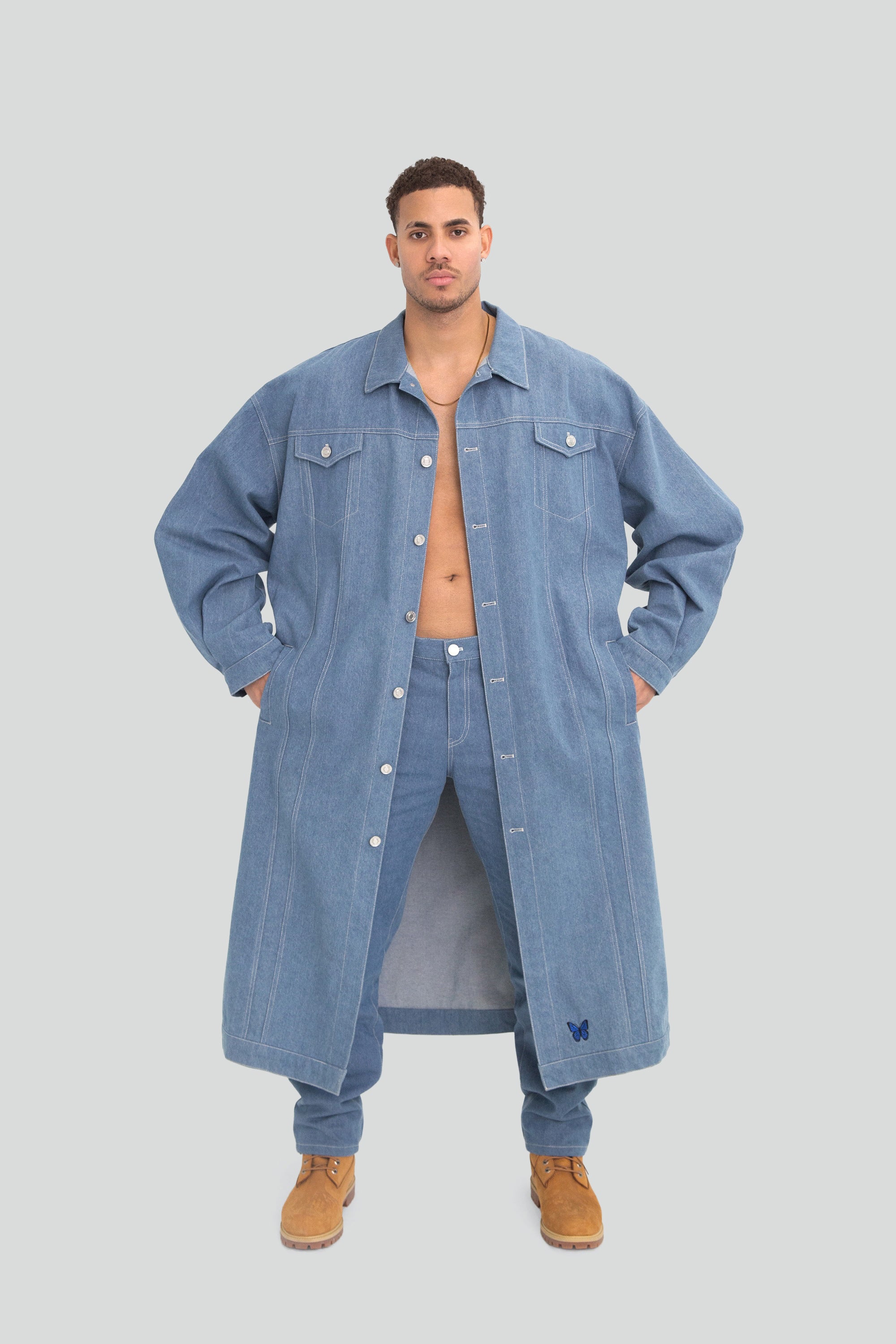 Man wearing a long oversized denim jacket and pants on a plain background