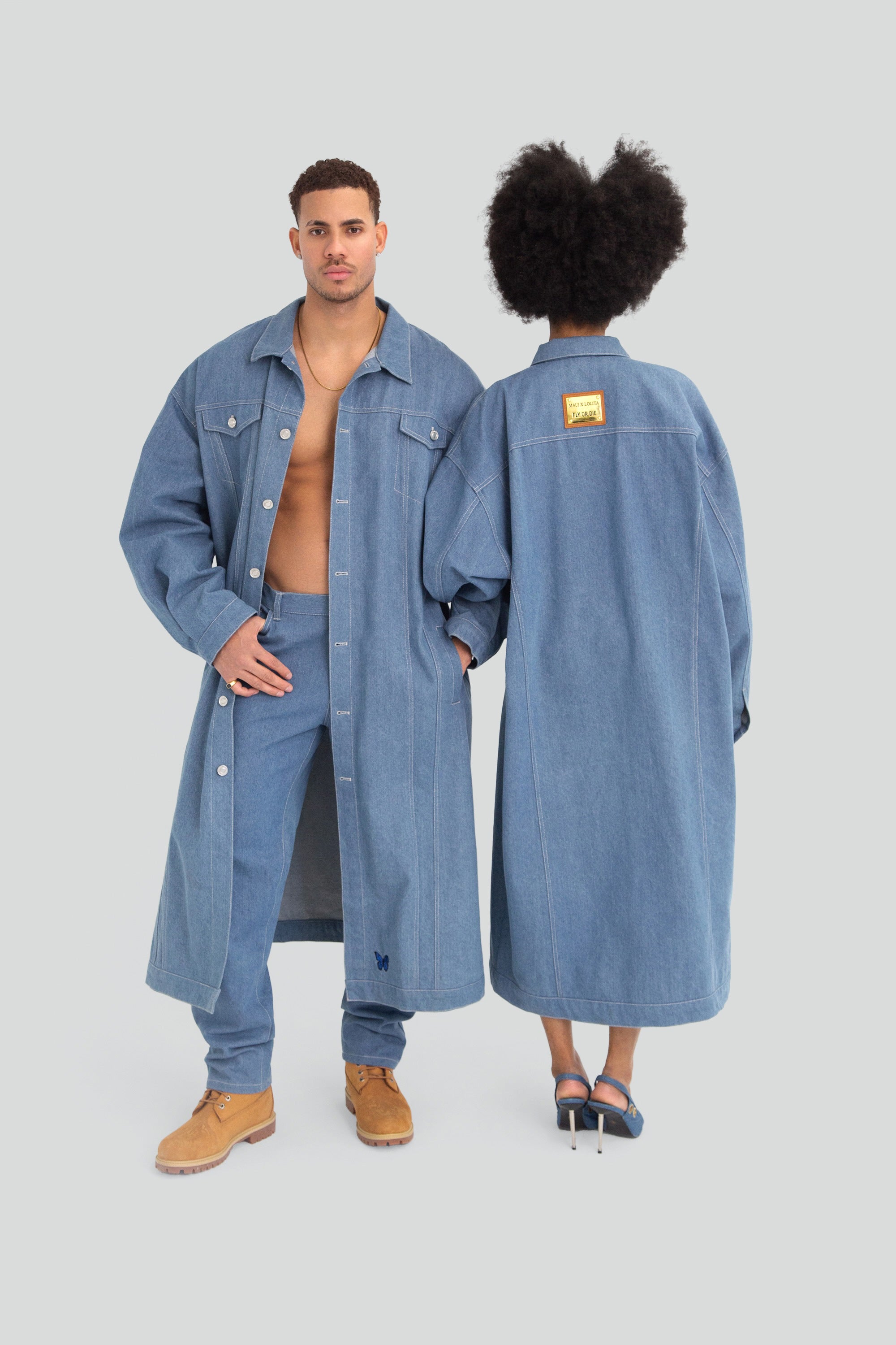 Two people wearing matching blue denim jackets on a plain background