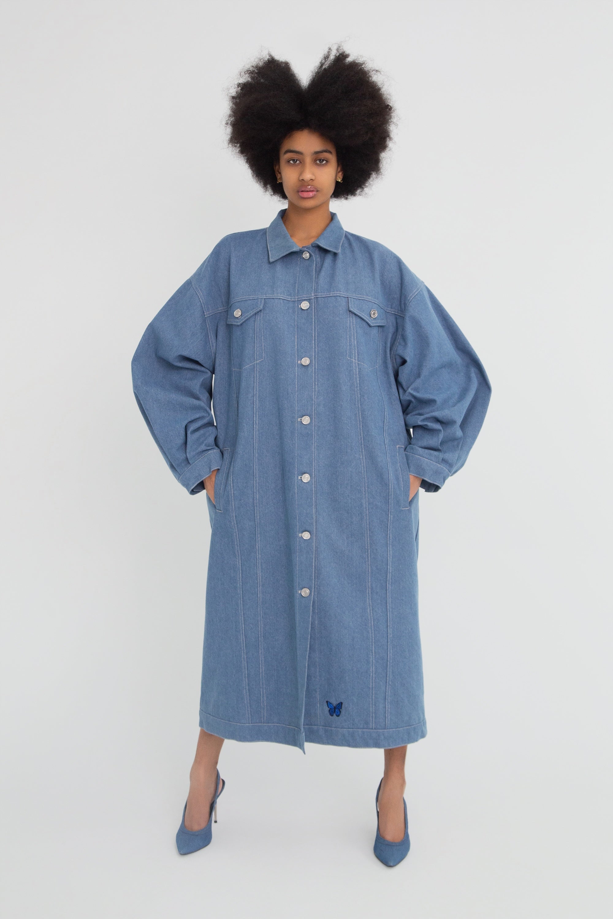 Woman wearing a long oversized denim jacket on a plain background.