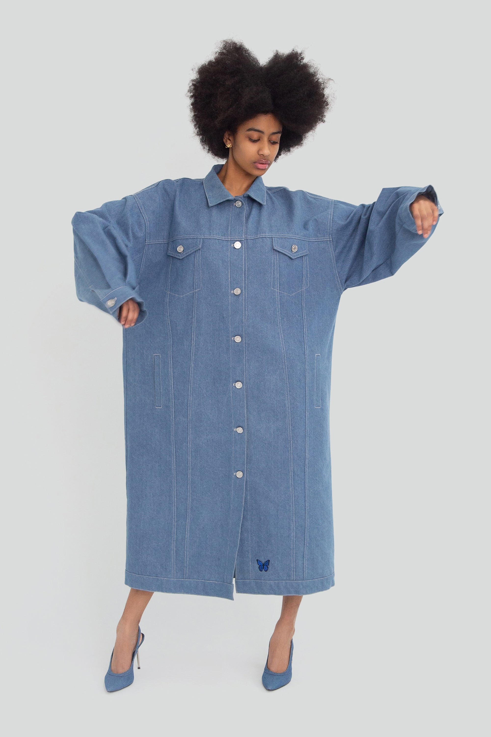 Woman wearing a long oversized denim jacket on a plain background.