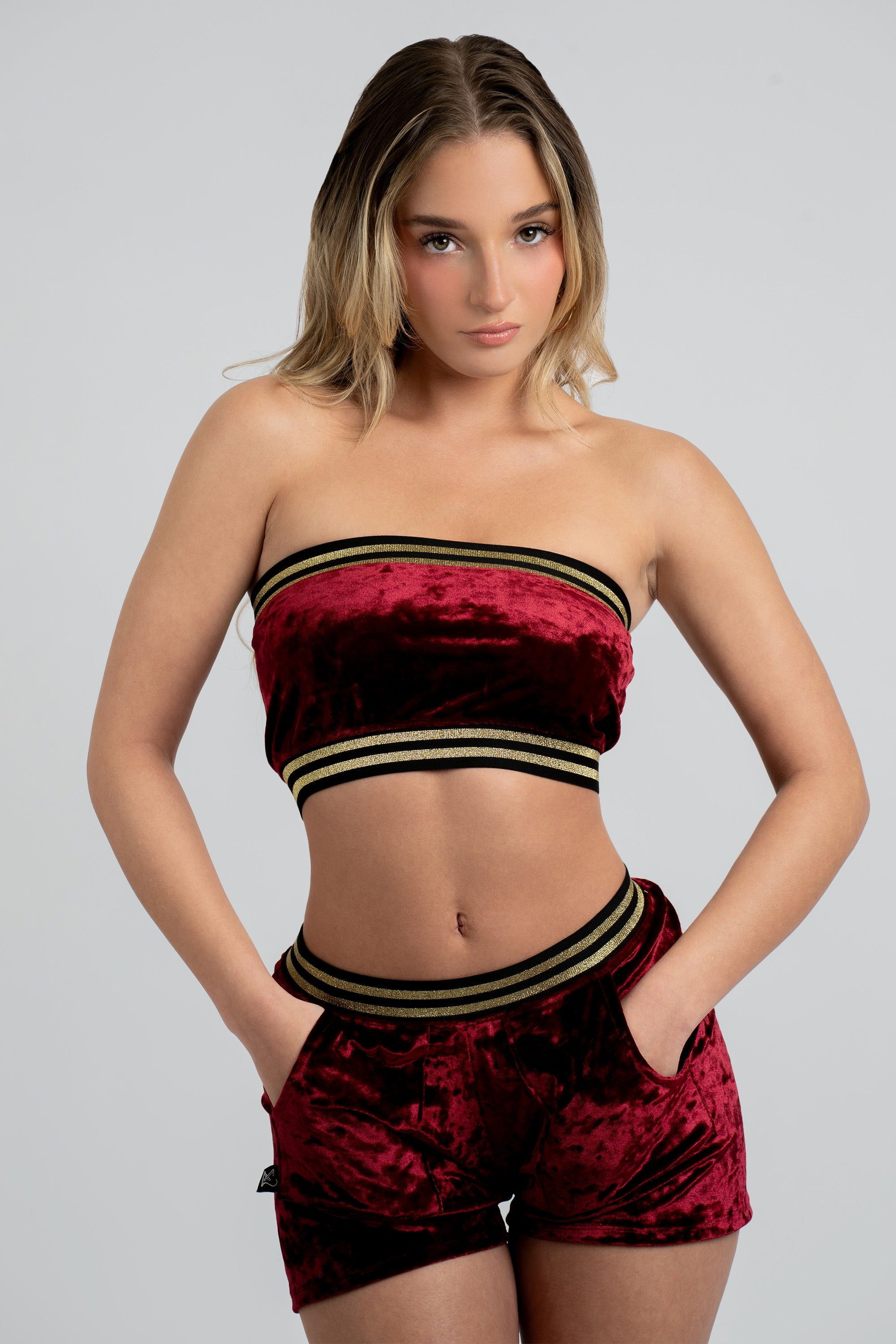 Woman wearing a red velvet bandeau top and matching shorts with a black and gold trim on a white background