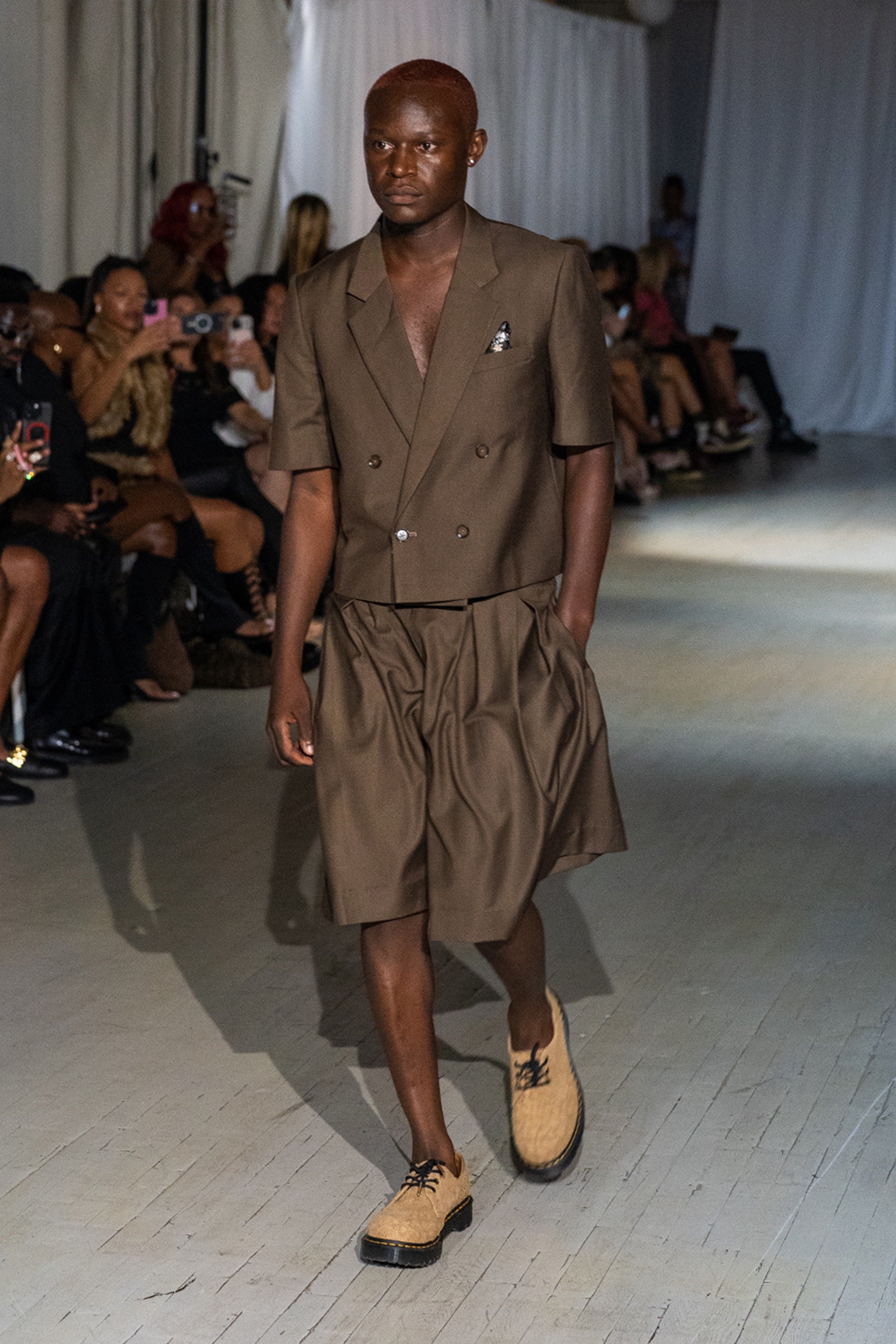 Model wearing a cropped brown blazer and short set walking down the runway.