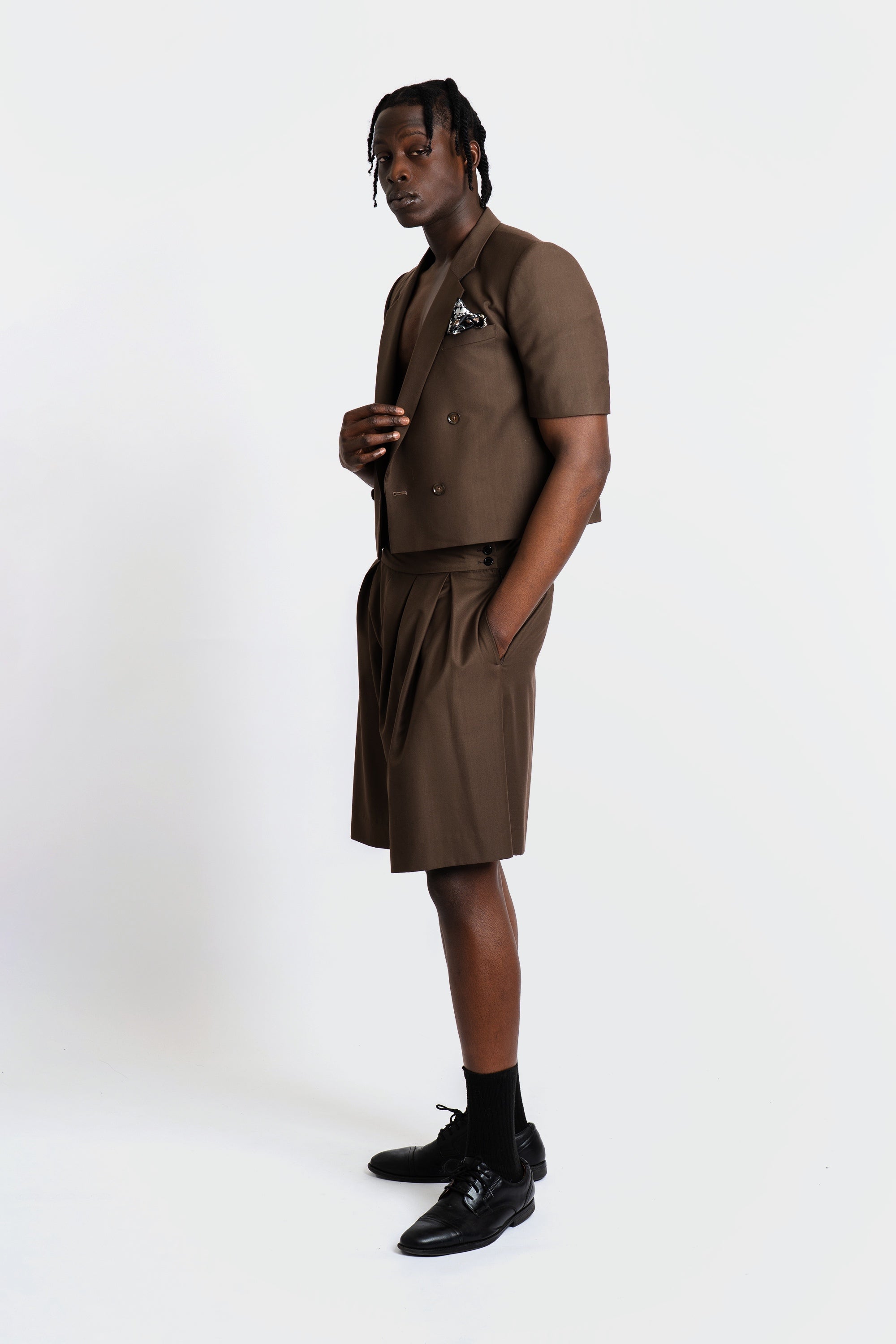 Man wearing a cropped brown blazer and short set on a white background.