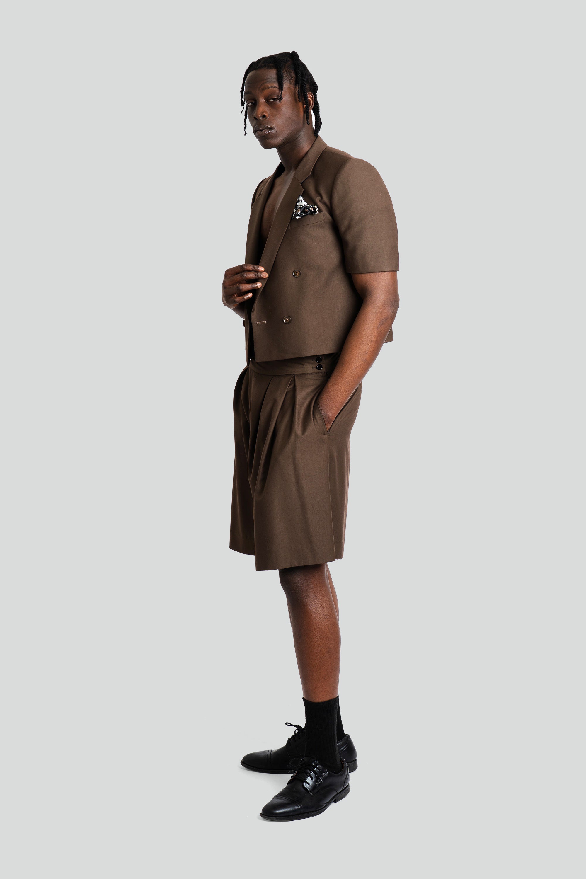 Man wearing a cropped brown blazer and short set on a white background.
