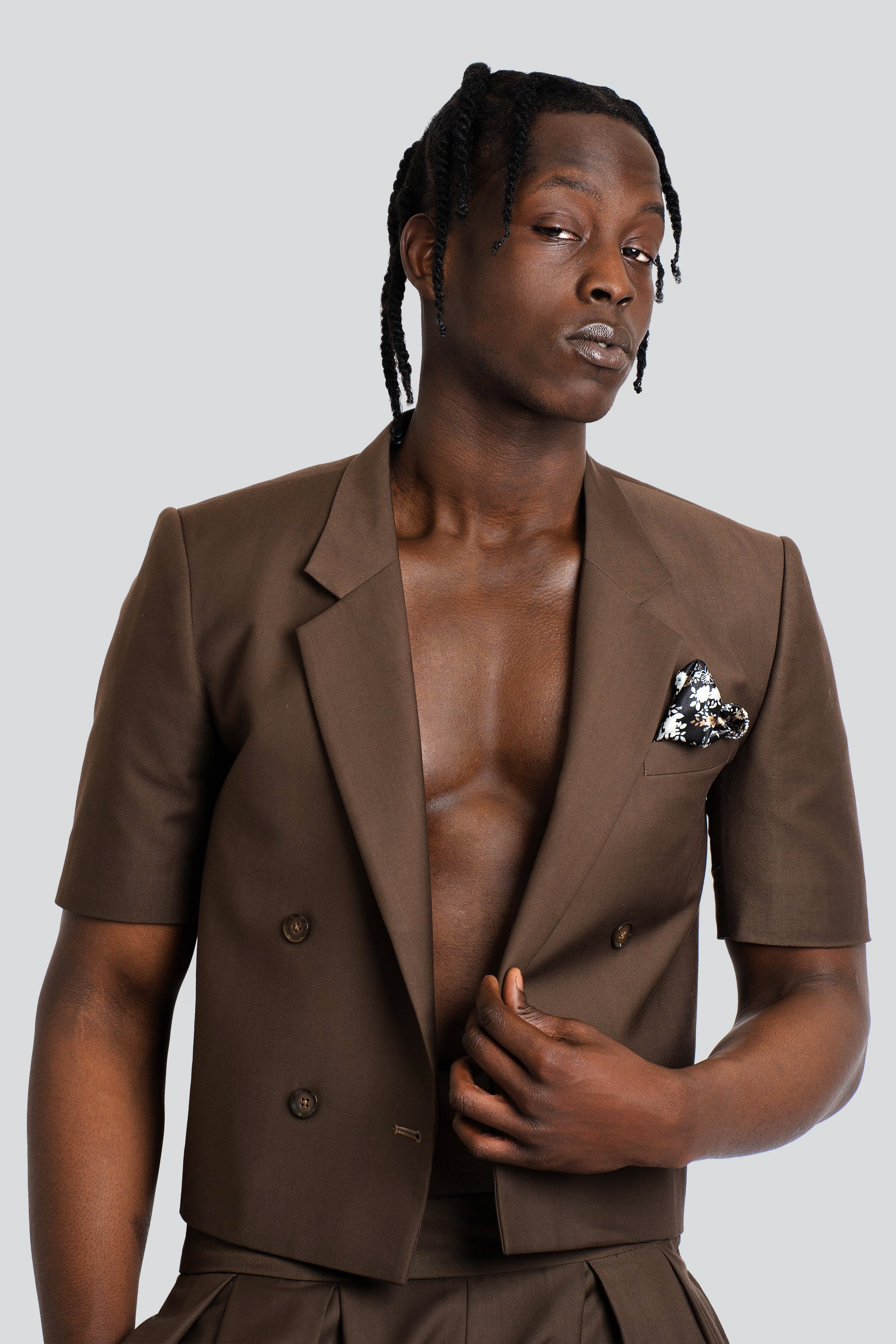 Man wearing a cropped brown blazer and short set on a white background.