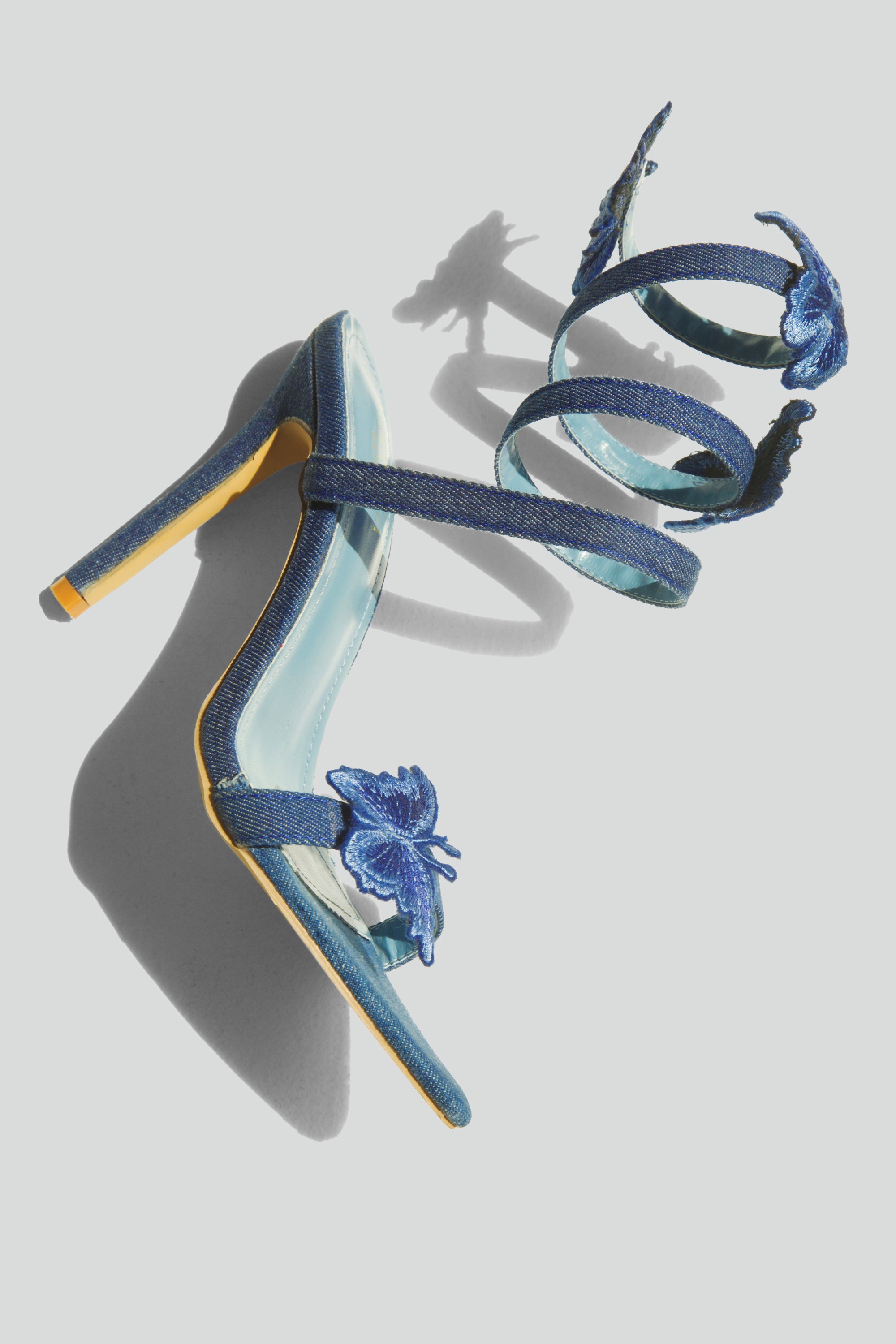 Blue high-heeled sandals with butterfly decorations on a light gray background