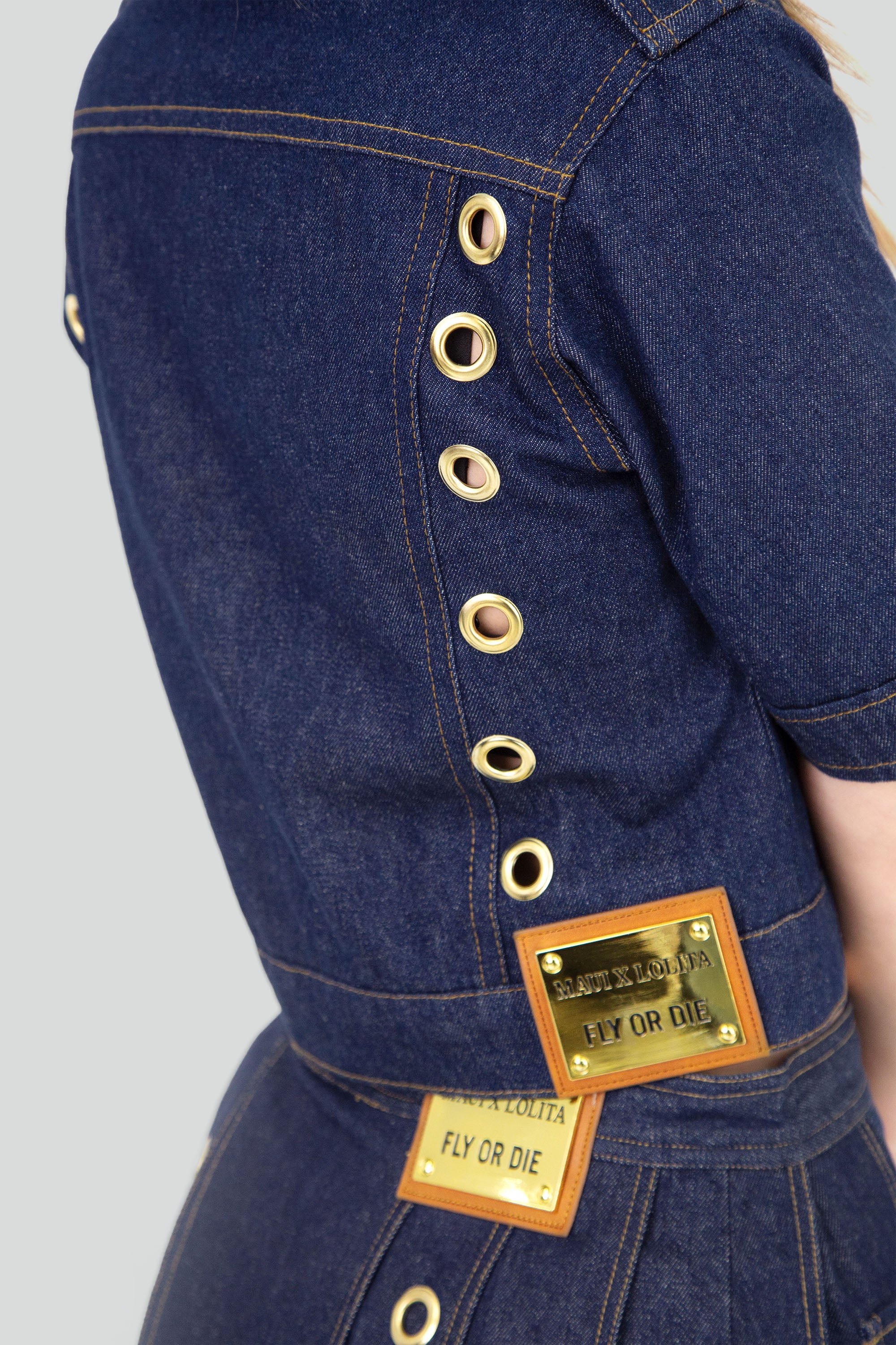 Denim jacket with gold grommets worn by a model on a plain background
