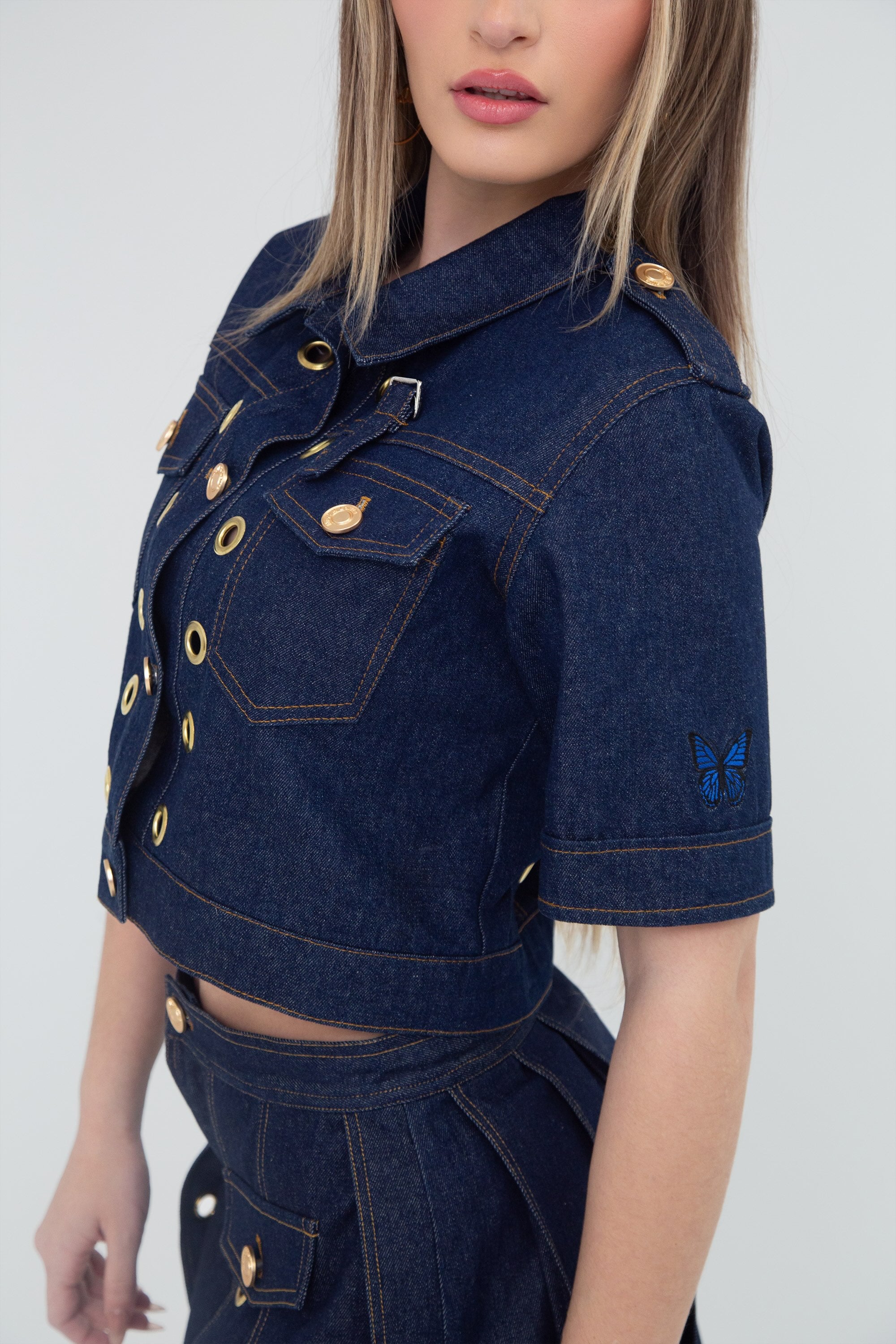 Denim jacket with gold grommets worn by a model on a plain background