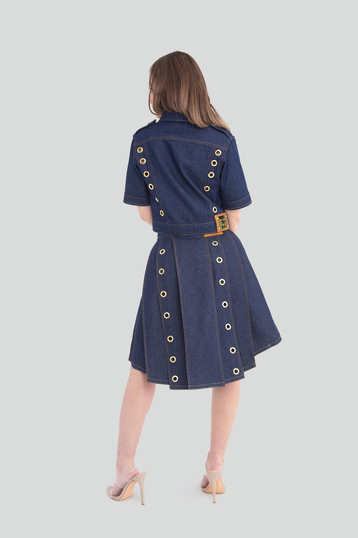 Back view of a matching dark wash indigo denim set featuring a structured cropped top and a pleated high waisted mini skirt