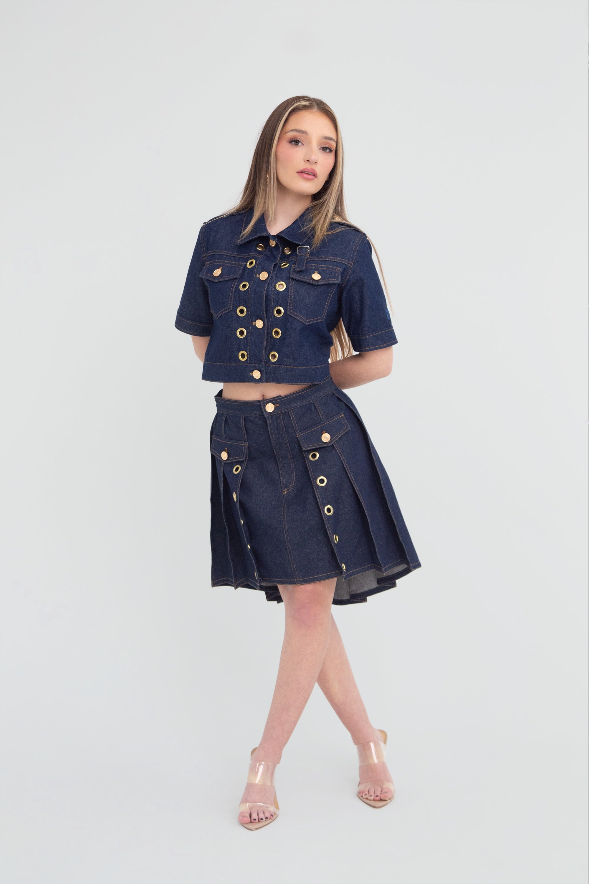 Woman wearing a denim outfit with gold grommets on a plain background