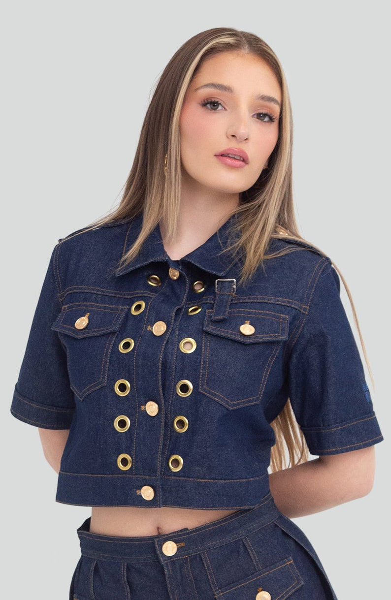 Woman wearing a denim outfit with gold grommets on a plain background