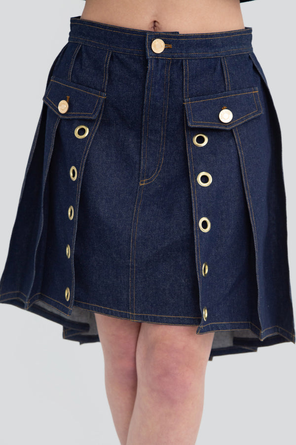 Close up view of a dark wash indigo denim pleated mini skirt highlighting the premium fabric texture and gold tone grommet details