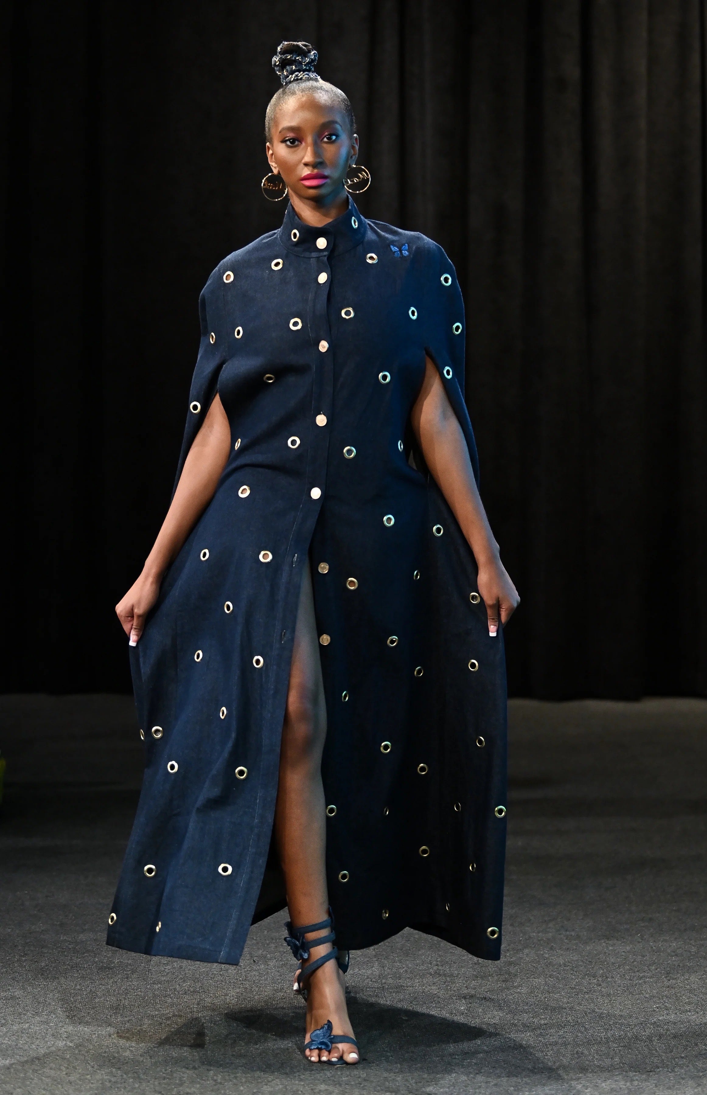 Woman wearing a dark blue dress with gold embellishments against a black background