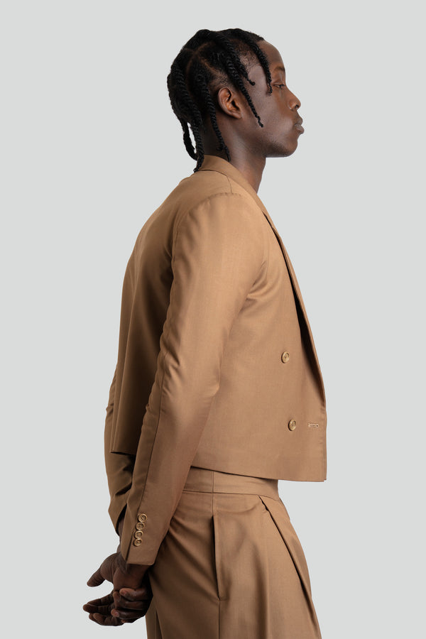 Studio portrait of a man wearing a light brown cropped suit featuring a short-cut double-breasted jacket and voluminous, deep-pleated wide-leg trousers