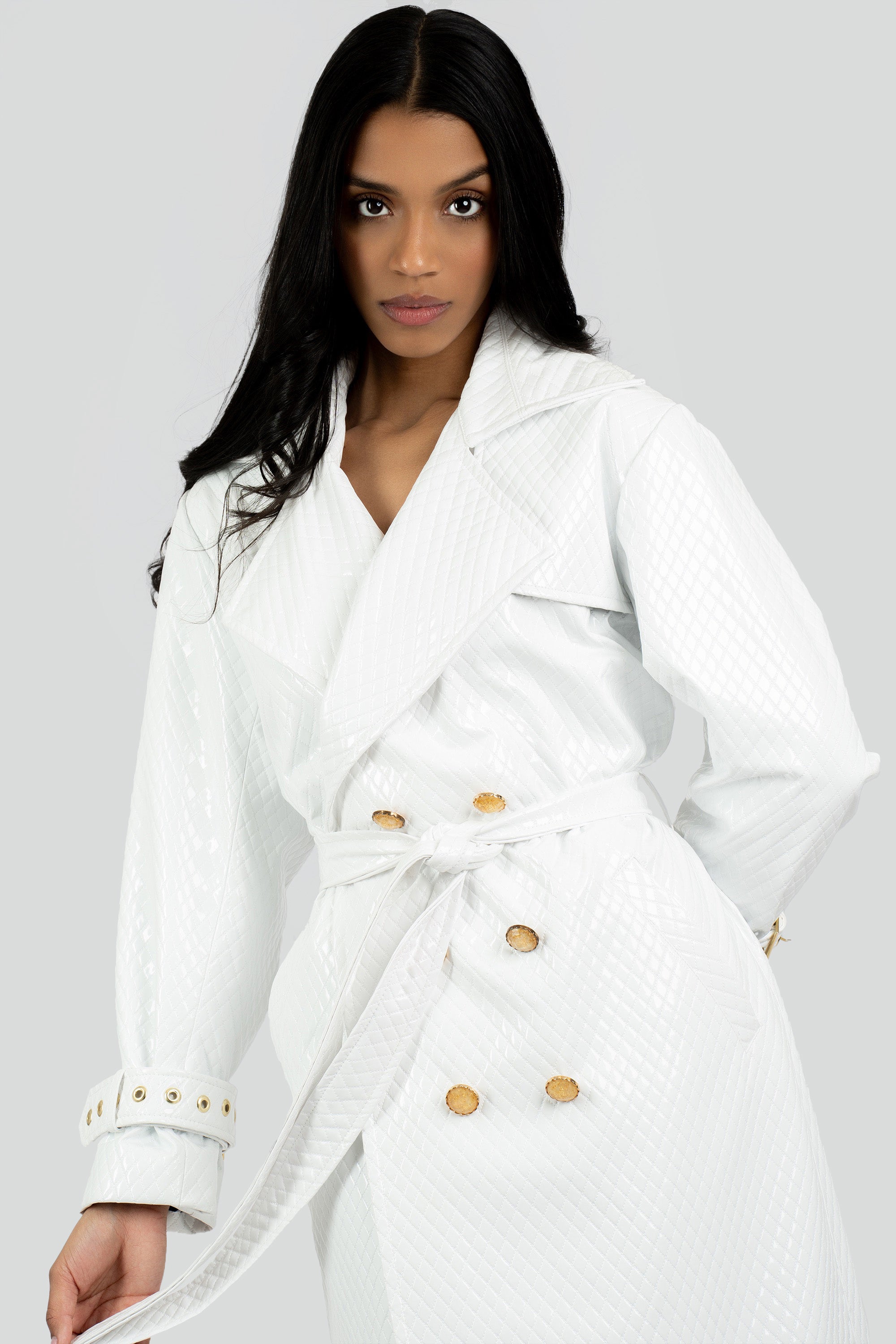 Woman wearing a white trench coat with gold buttons on a gray background