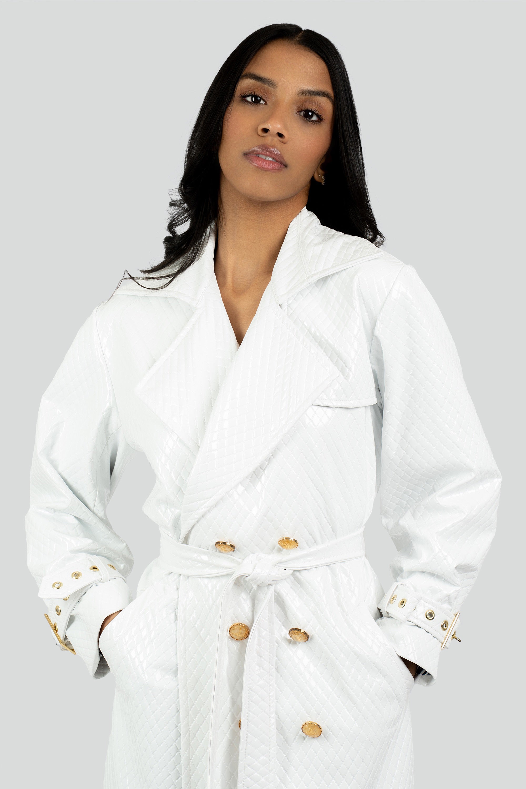 Woman wearing a white trench coat with gold buttons on a gray background