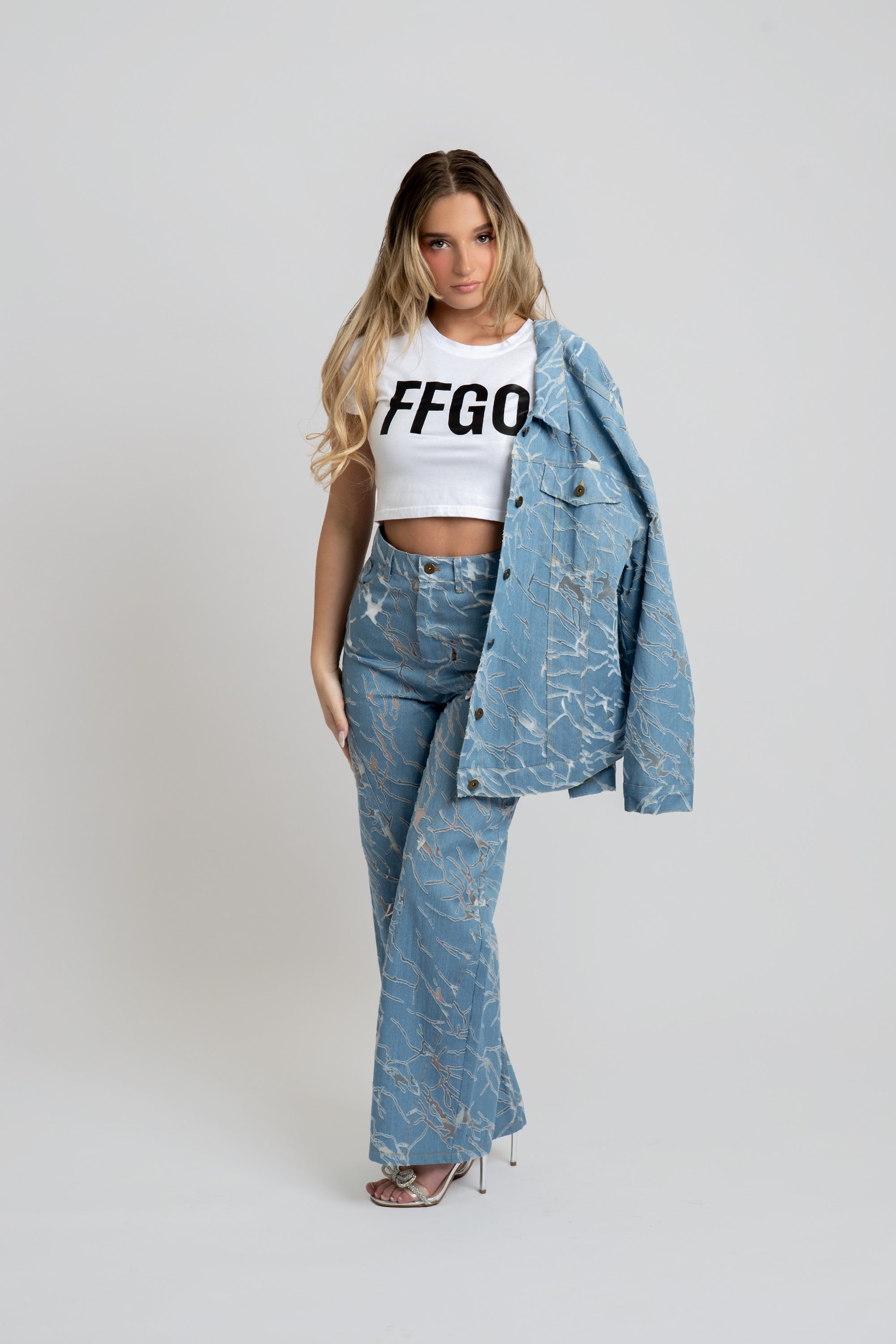 Woman wearing a white crop top with 'FFGO' text, blue denim jacket, and jeans on a white background
