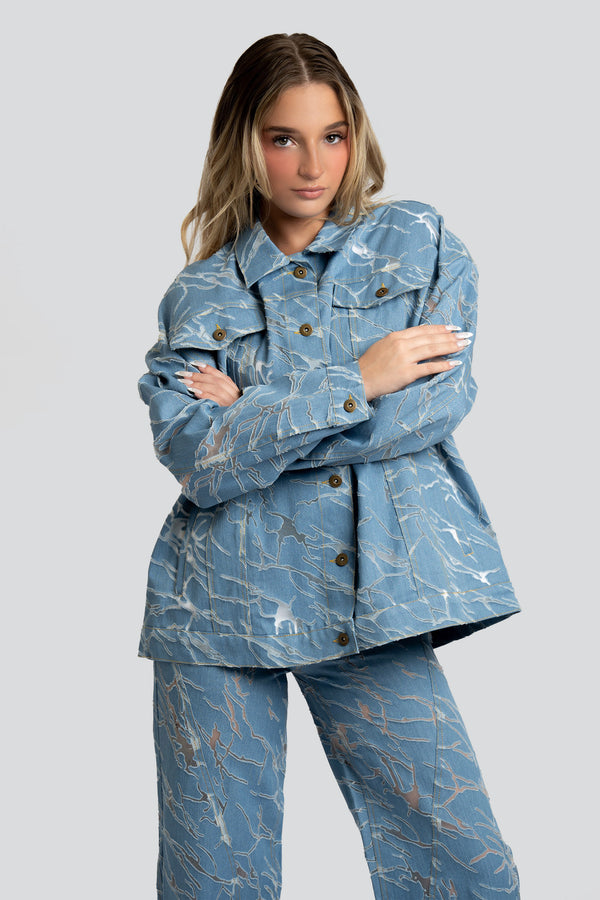 Close-up of a blue marbled mesh and structured cotton denim fabric layout highlighting asymmetric flap pockets and fine gold-tone hardware