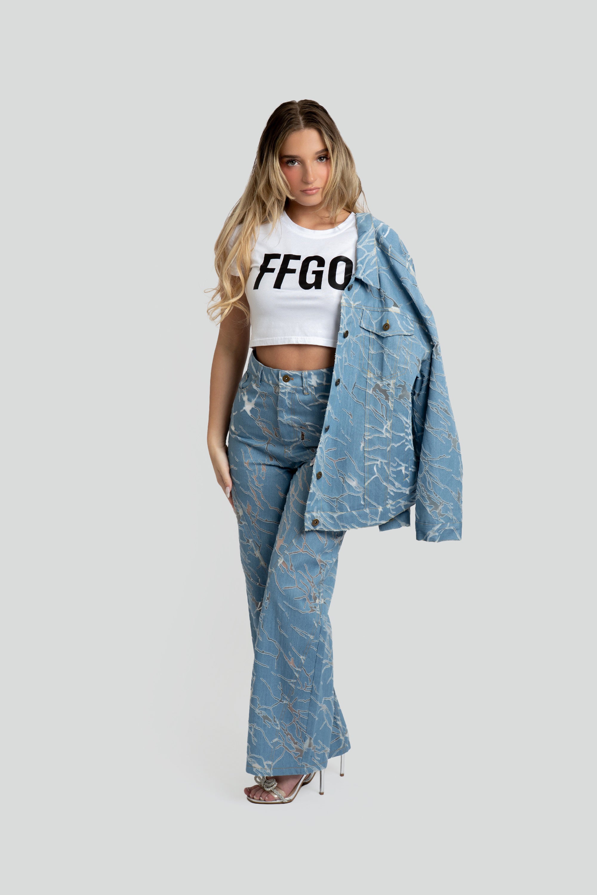 Woman wearing a white crop top with 'FFGO' text, blue denim jacket, and jeans on a white background