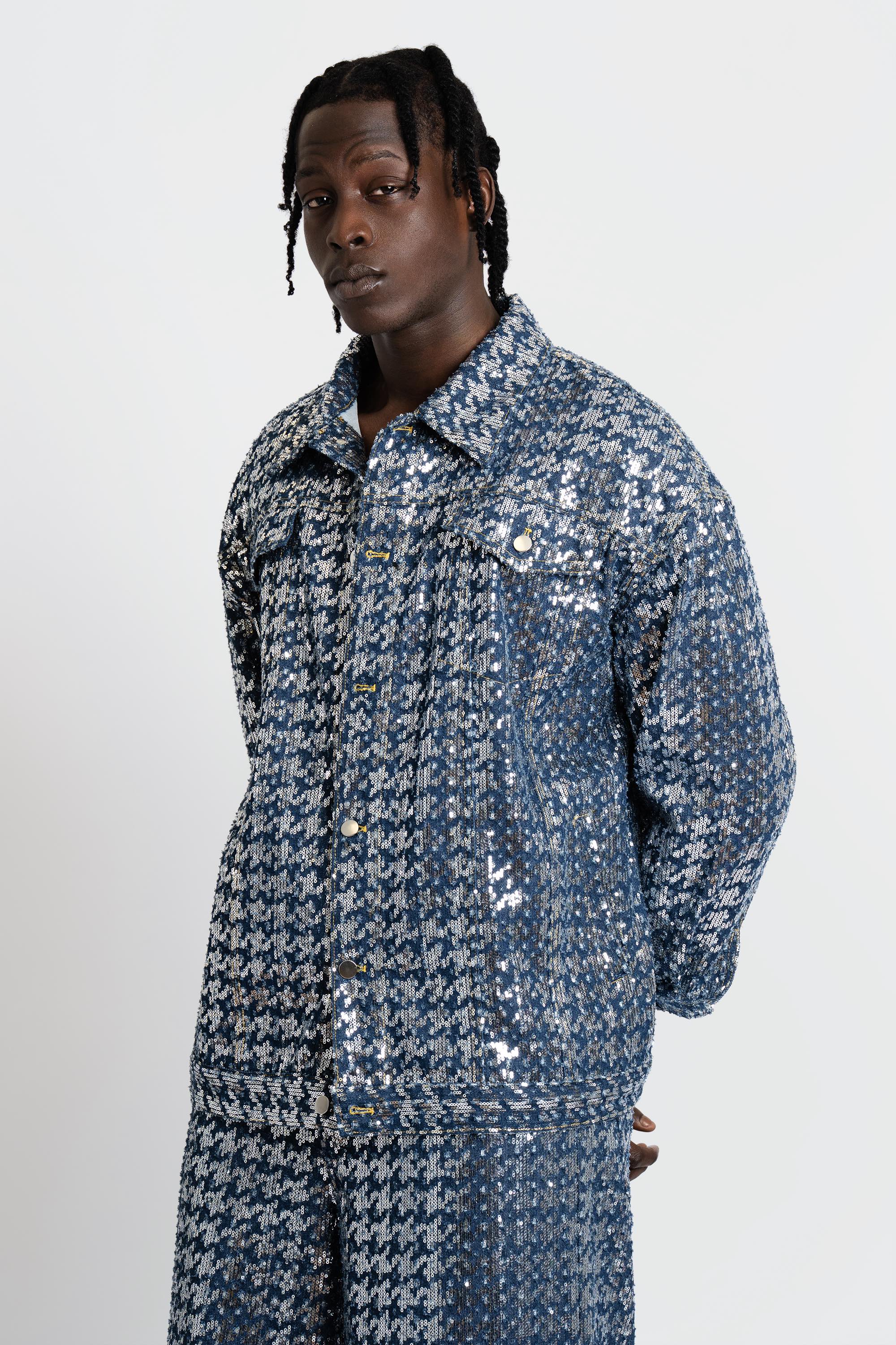 Man wearing a blue sequined denim set on a white background.