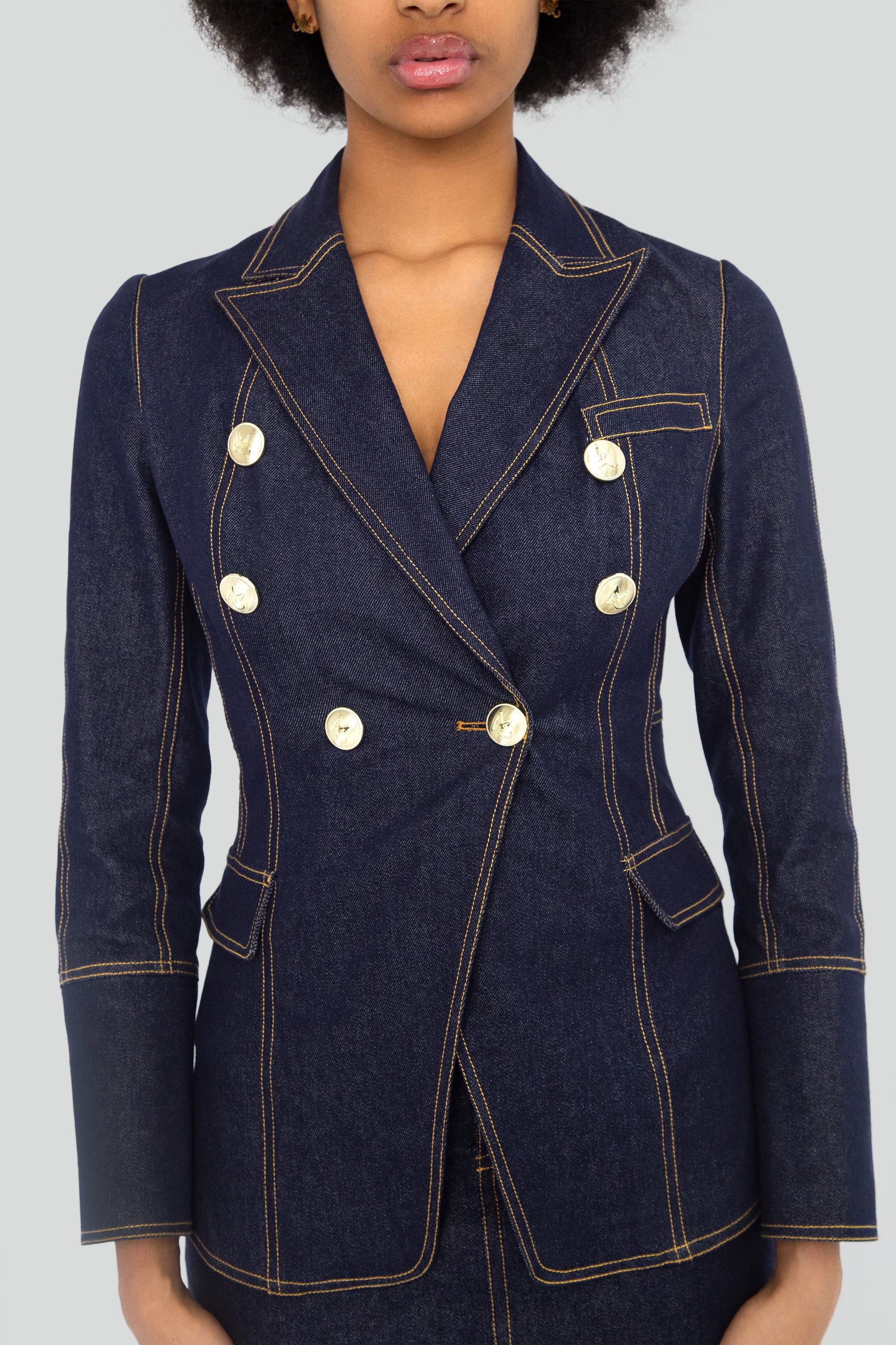 Woman wearing a dark denim blazer with gold buttons on a plain background