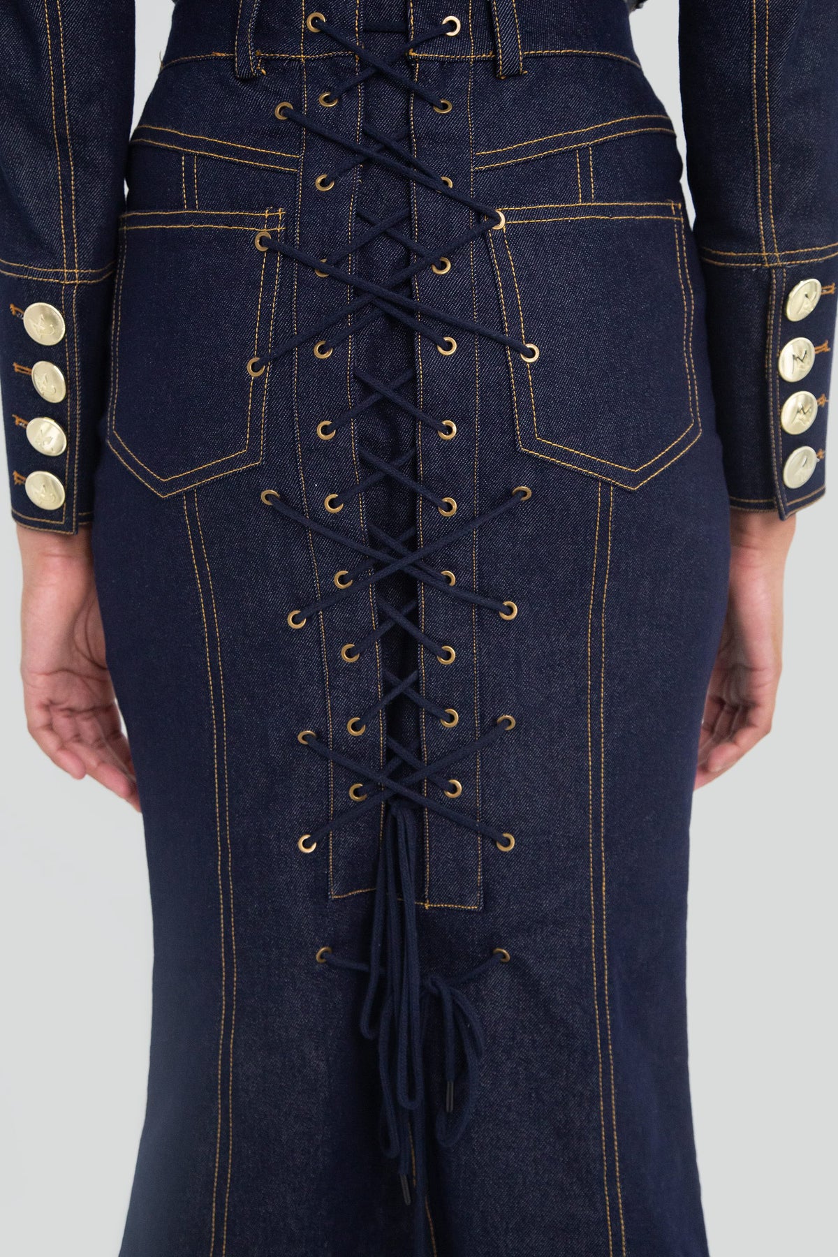 Close up view of a high waisted dark indigo denim pencil skirt highlighting the sharp contrast topstitching and premium woven fabric texture