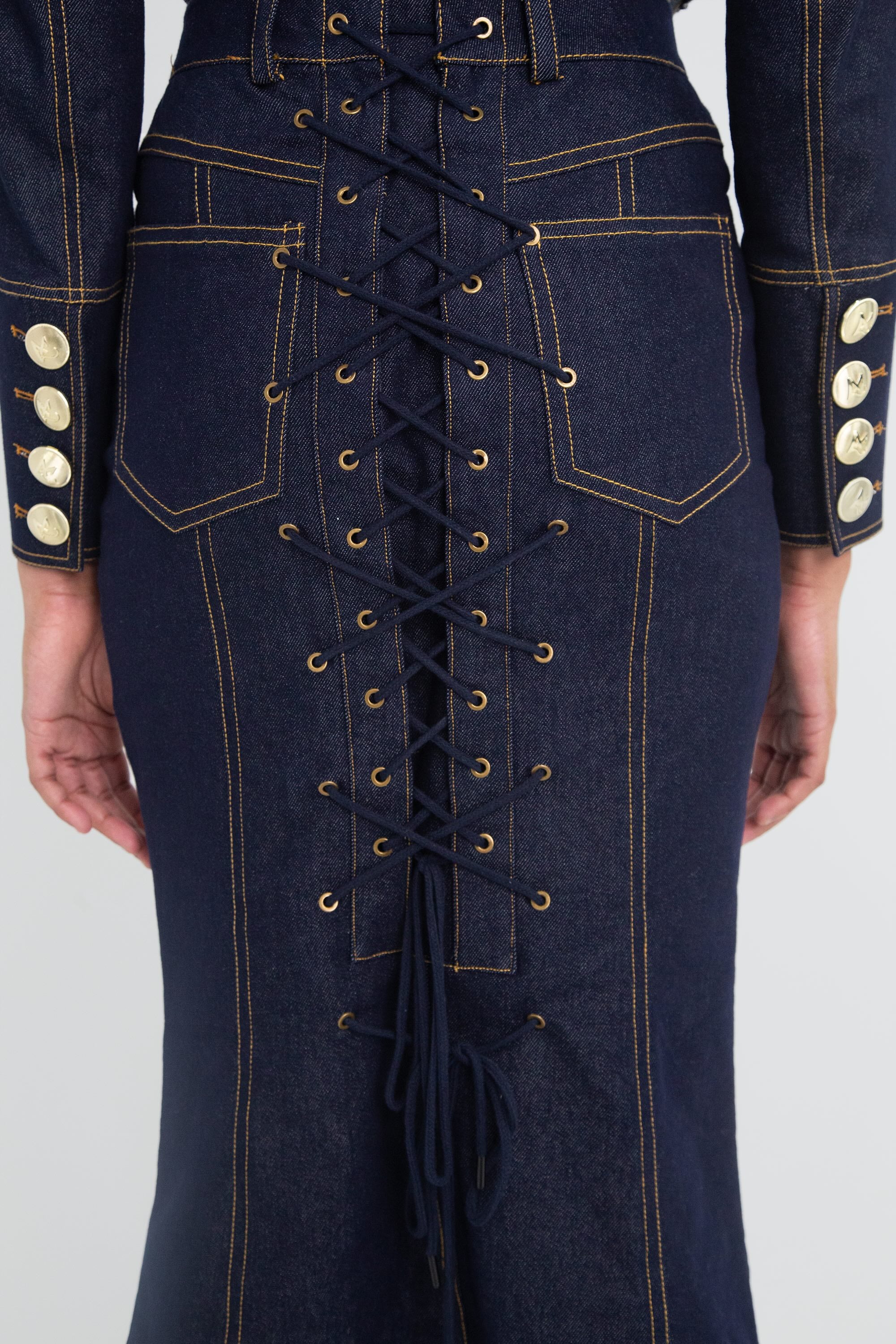 A dark denim skirt with a corset lace worn by a model on a plain background