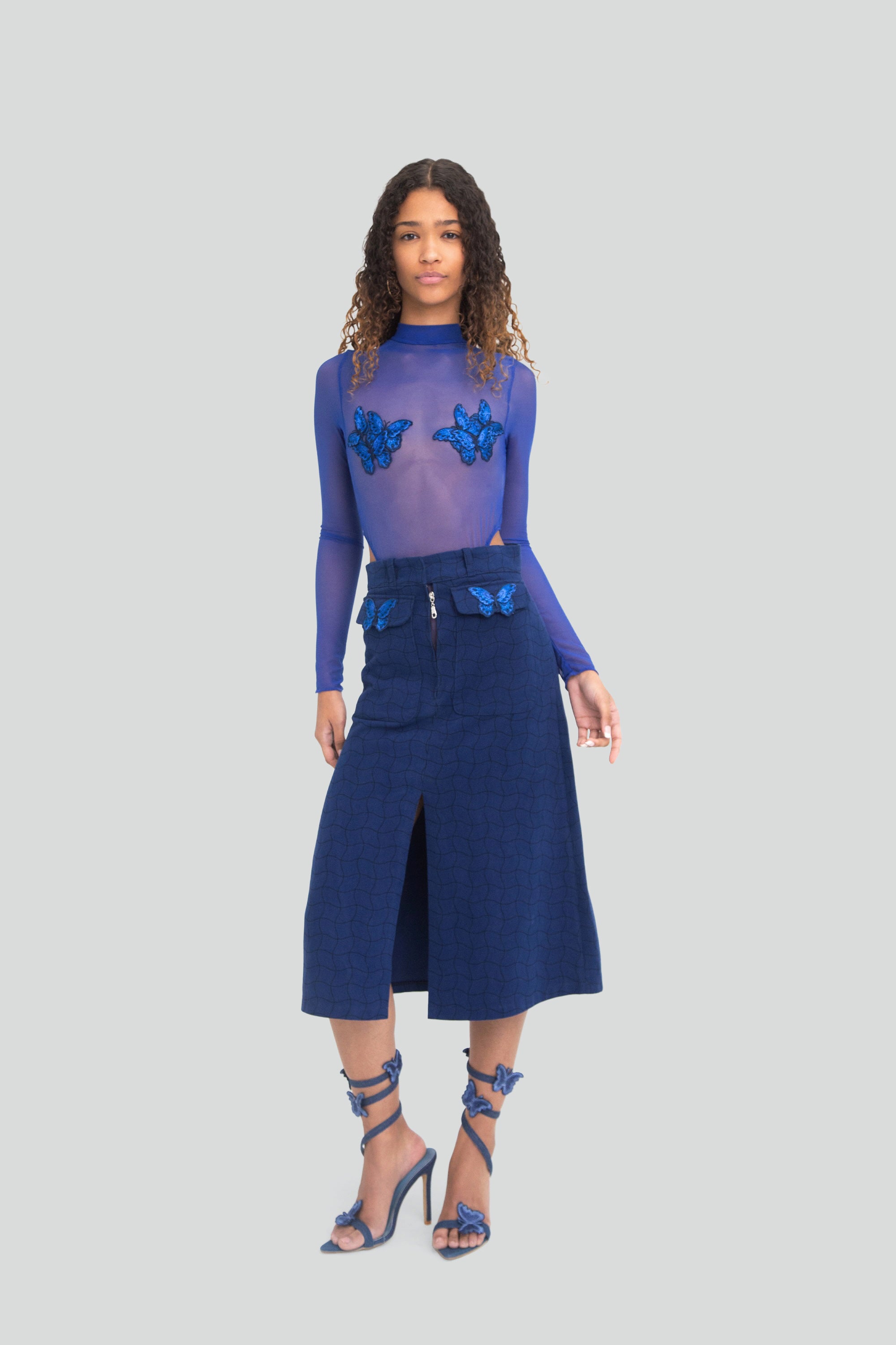 Woman wearing a blue outfit with butterfly details on a plain background