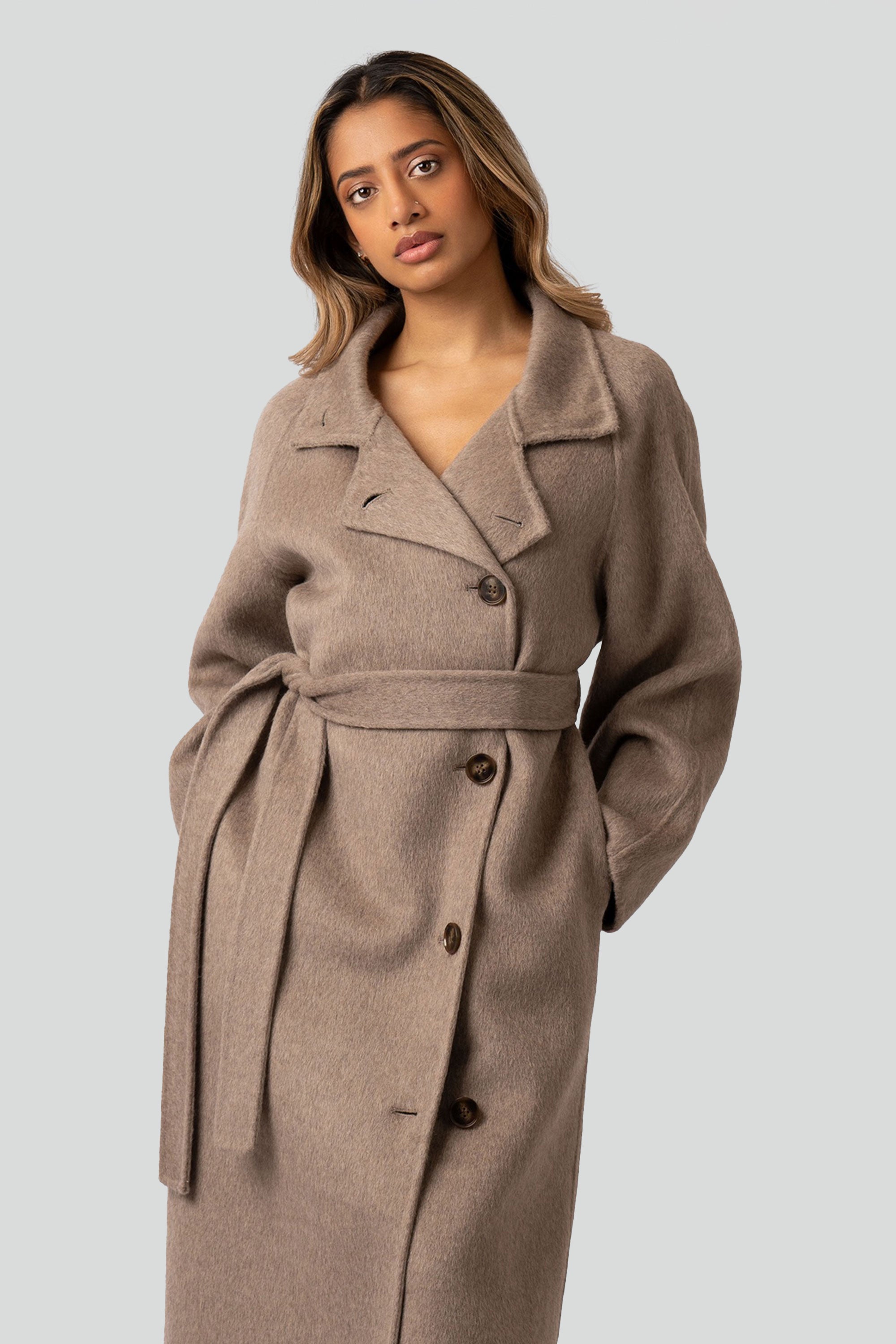 Woman wearing a beige wool coat with buttons and belt on a white background