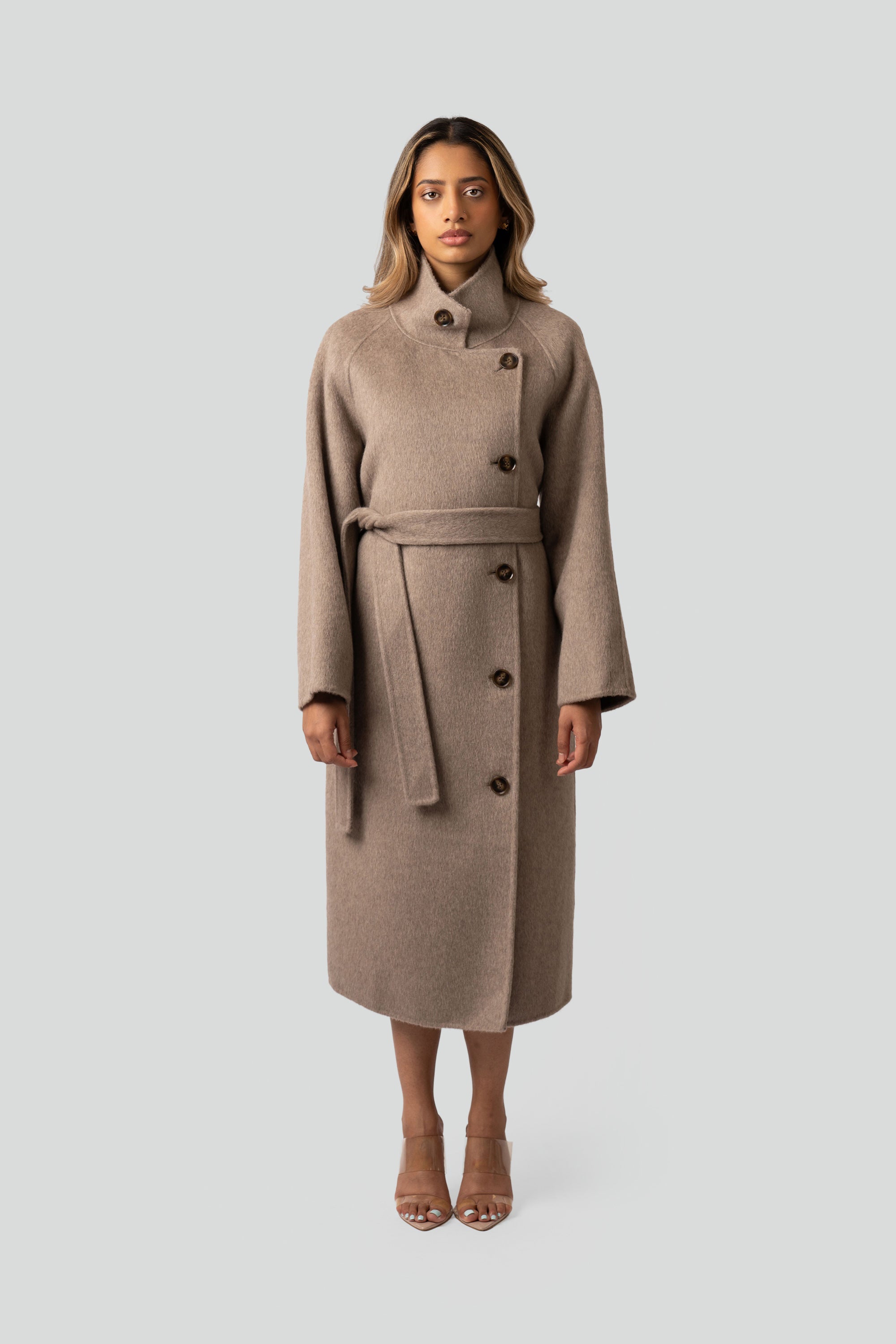 Woman wearing a beige wool coat with buttons and belt on a white background