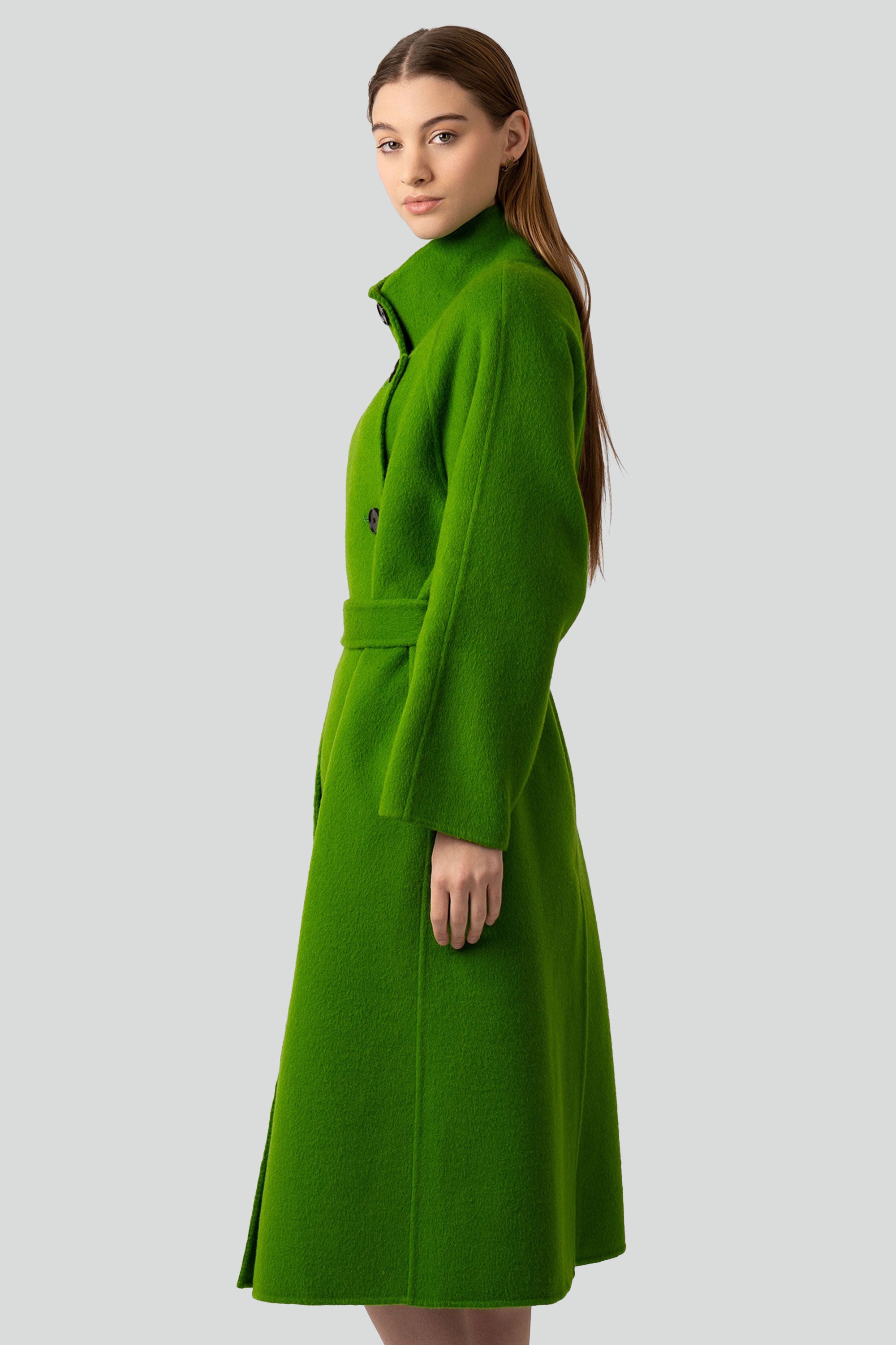 Woman wearing a green wool coat with buttons and belt on a white background