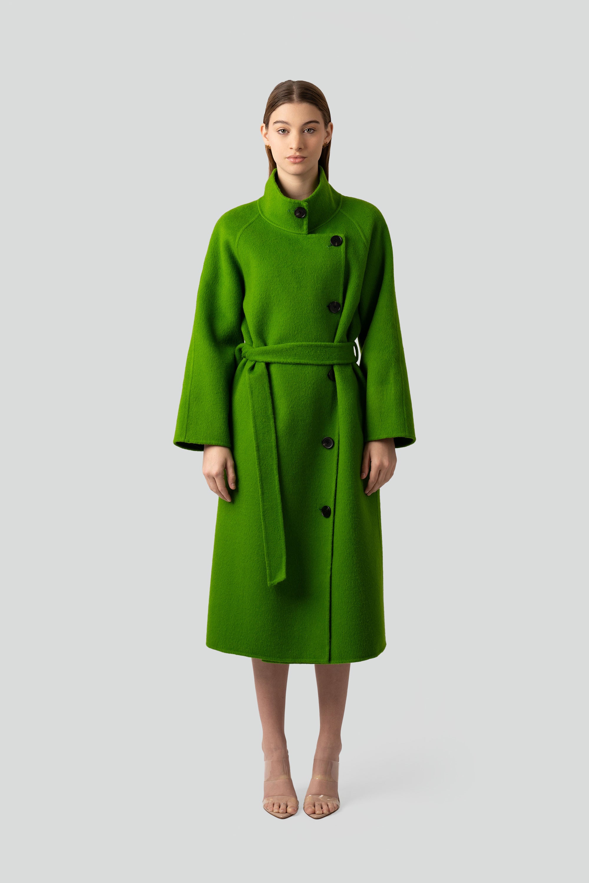 Woman wearing a green wool coat with buttons and belt on a white background
