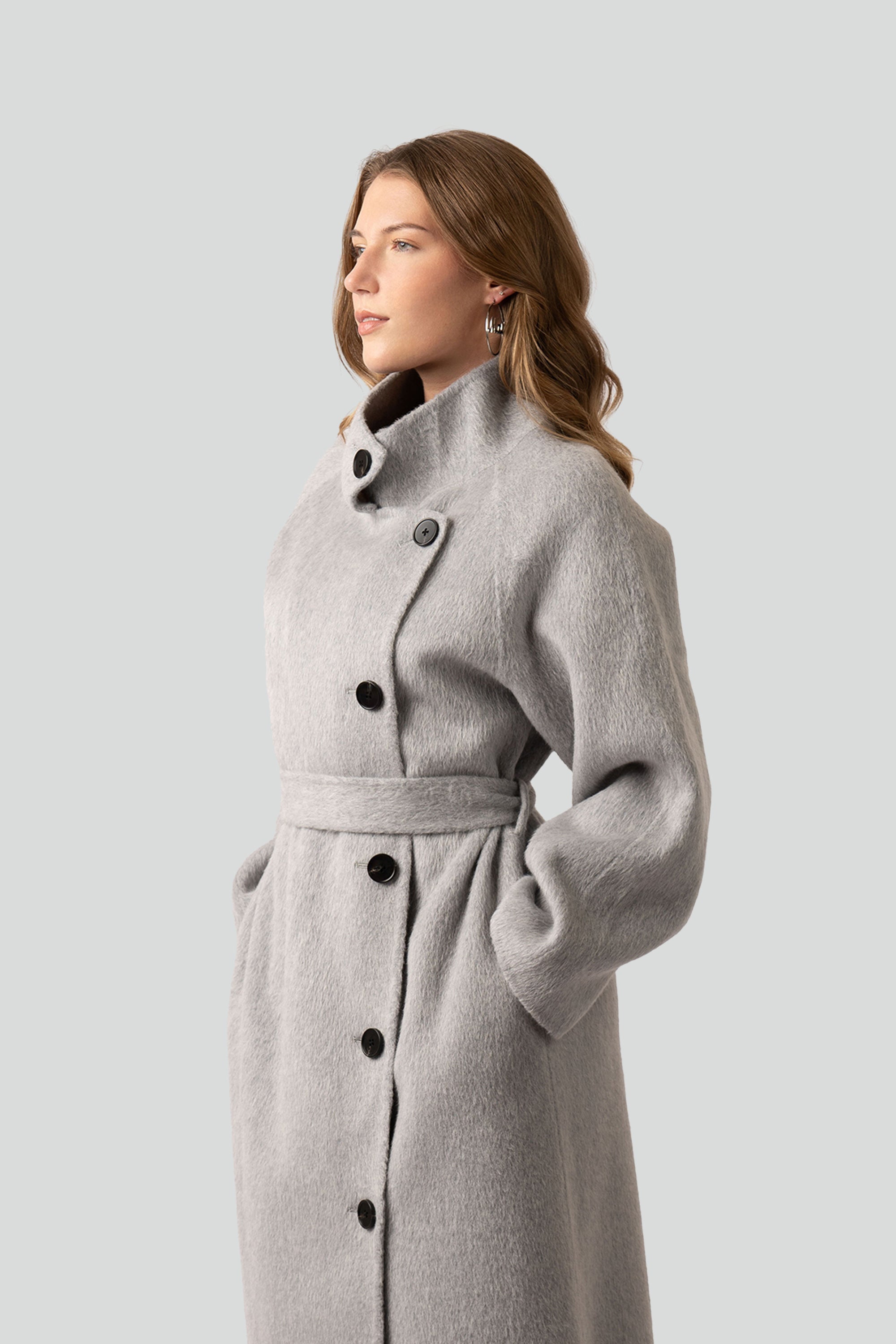 Woman wearing a gray wool coat with buttons and belt on a white background