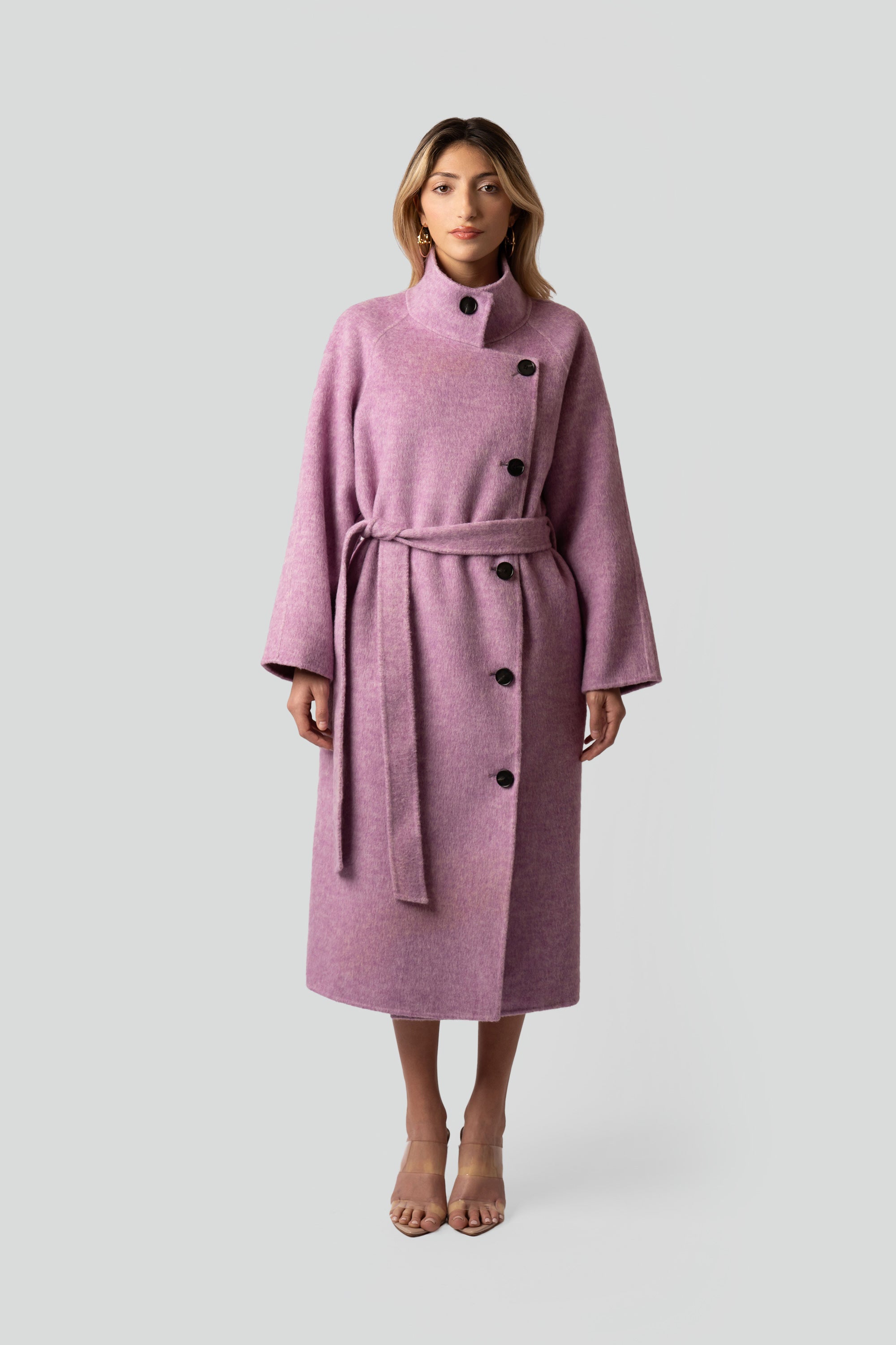 Woman wearing a pink wool coat with buttons and belt on a white background