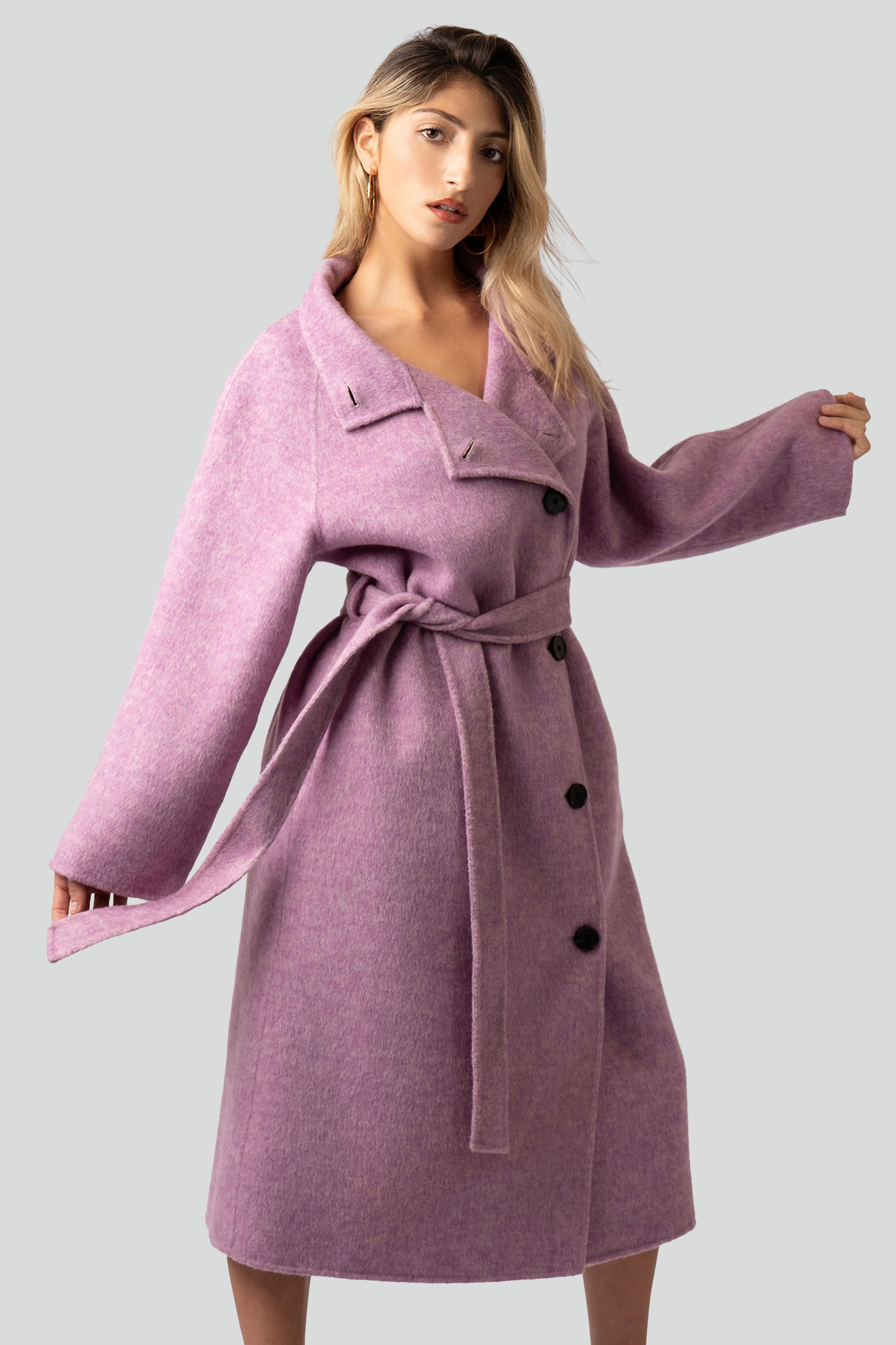 Woman wearing a pink wool coat with buttons and belt on a white background