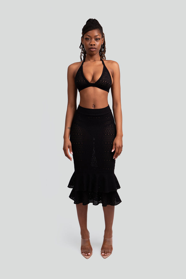 Woman wearing a black lace knit matching set featuring a triangle halter bralette top and a ruffled midi skirt