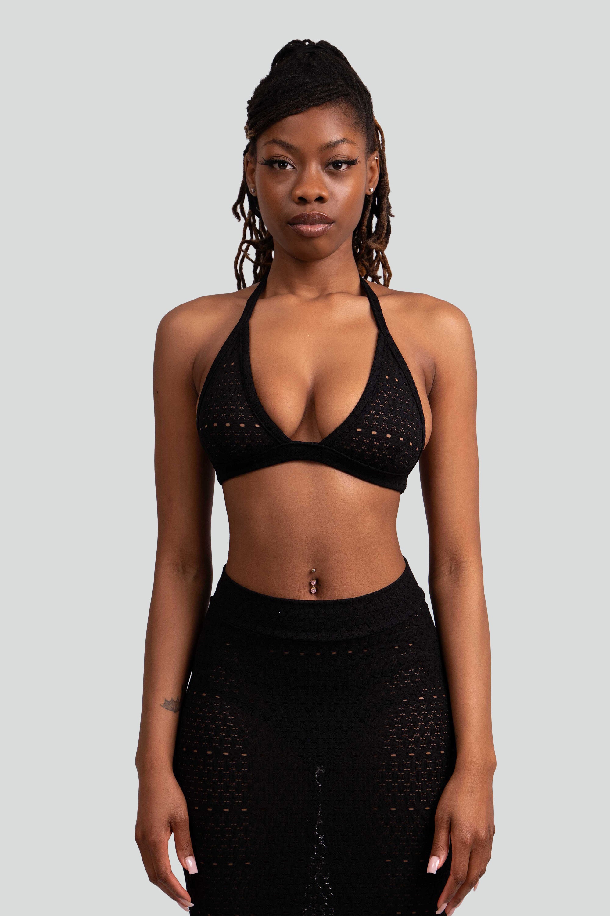Close up of a woman wearing a black lace knit outfit with a halter top and ruffled skirt on a white background